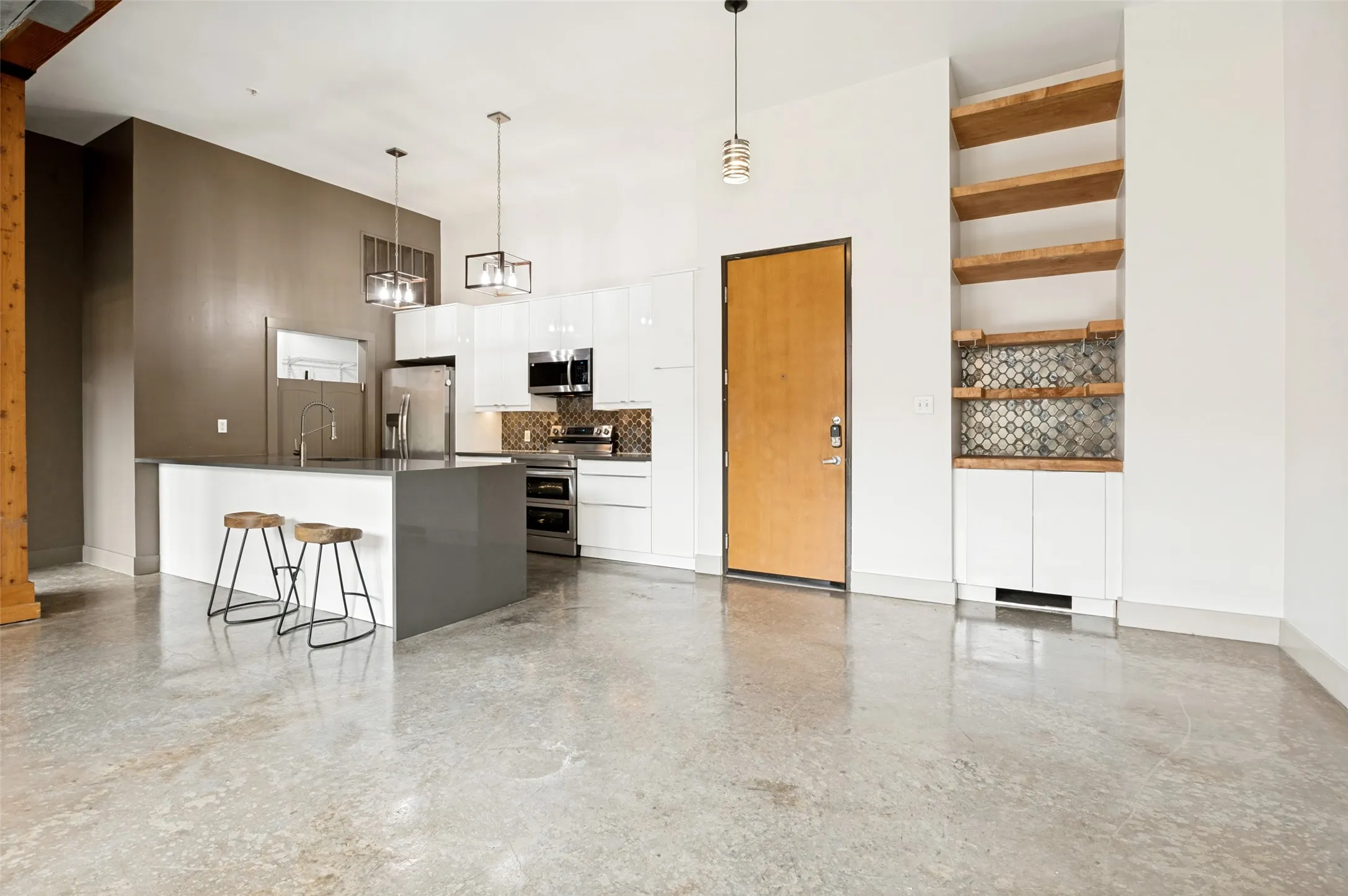 Polished concrete flooring with a modern kitchen featuring an island, stainless steel appliances, white cabinetry, plus a dry bar by the dining area