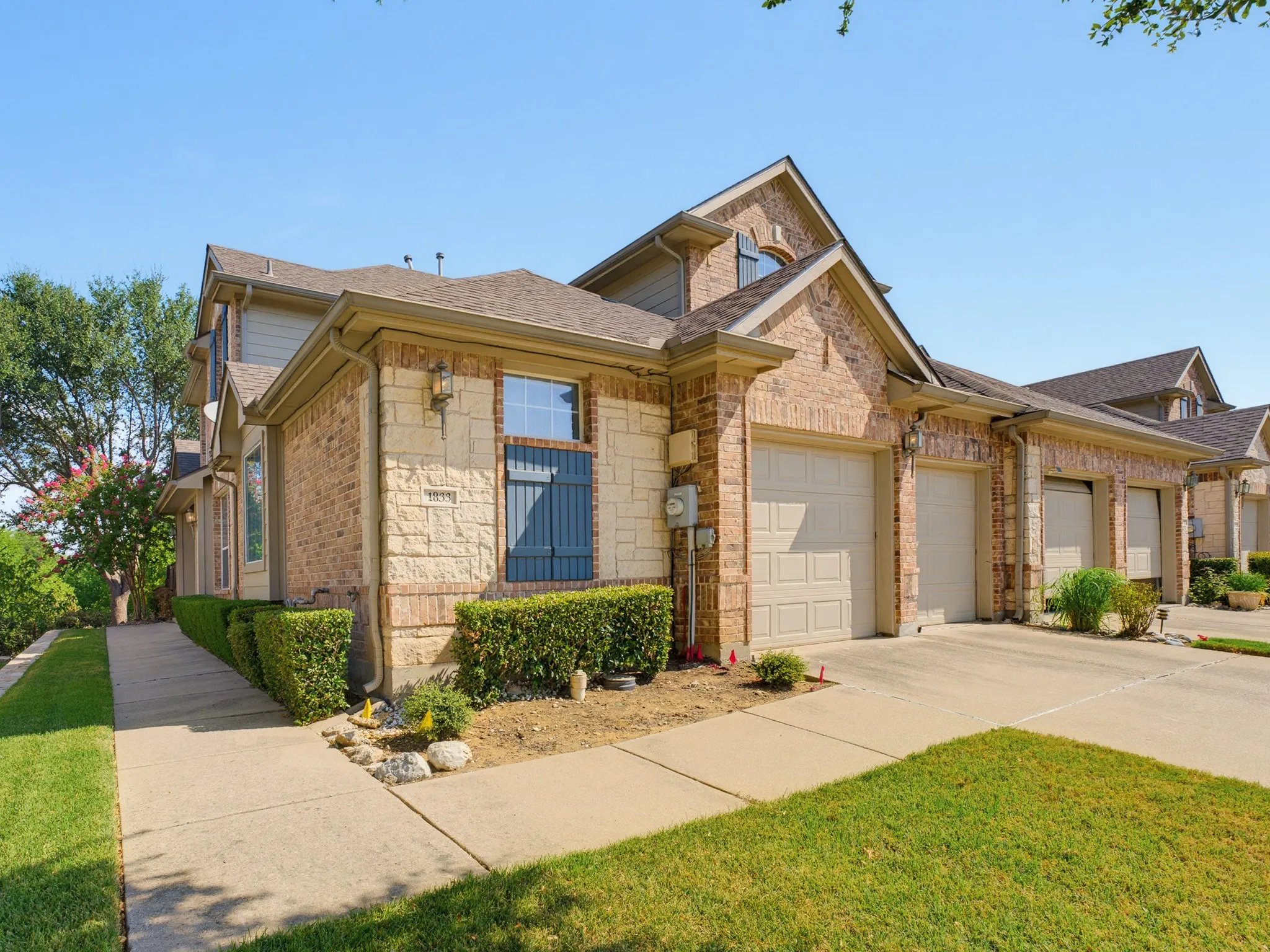 Brick and stone exterior with multiple garage bays, individual driveways, and manicured landscaping