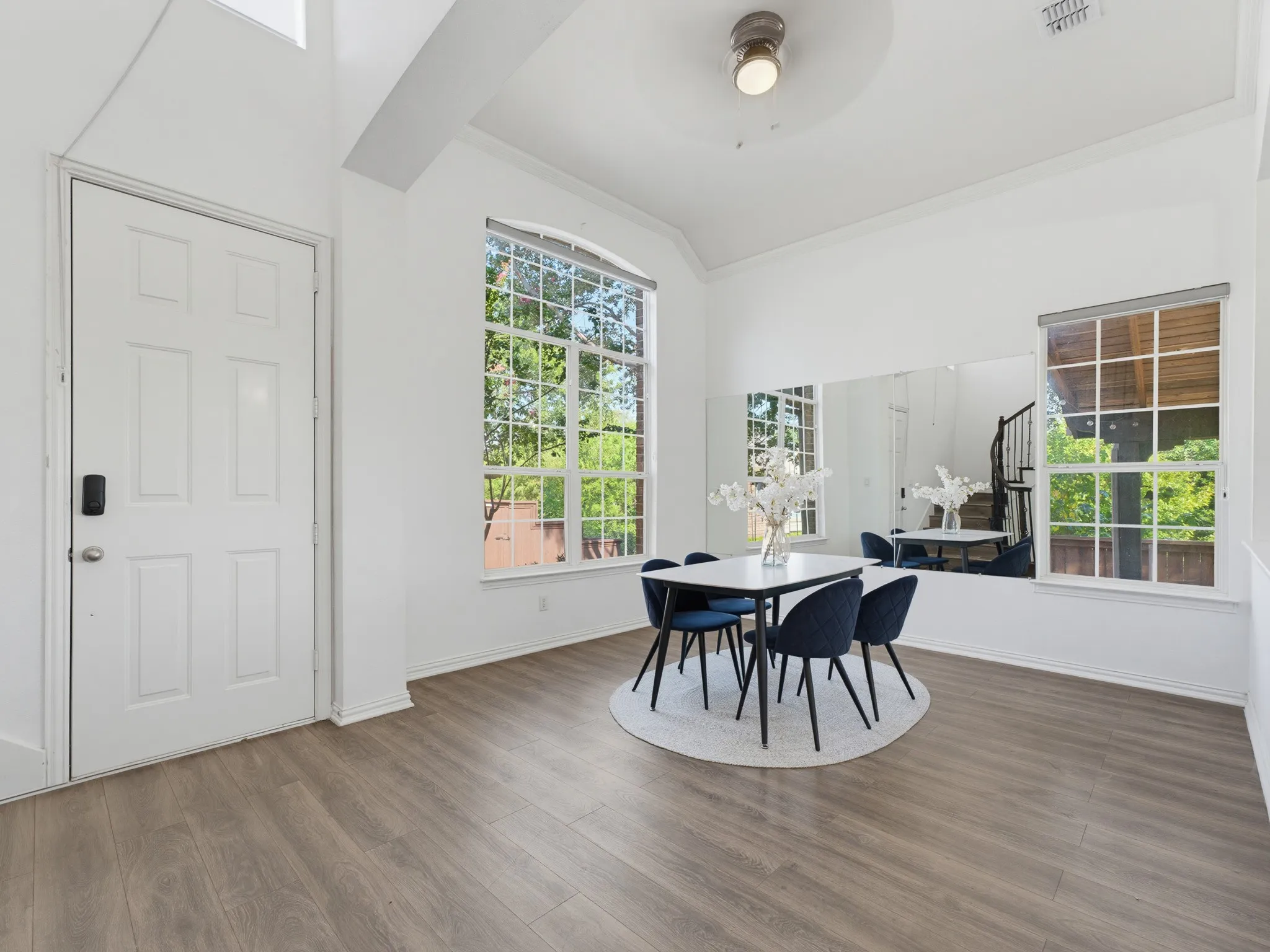 Wood-finish flooring, high ceilings, large arched window, multiple rectangular windows, and a flush mount ceiling light
