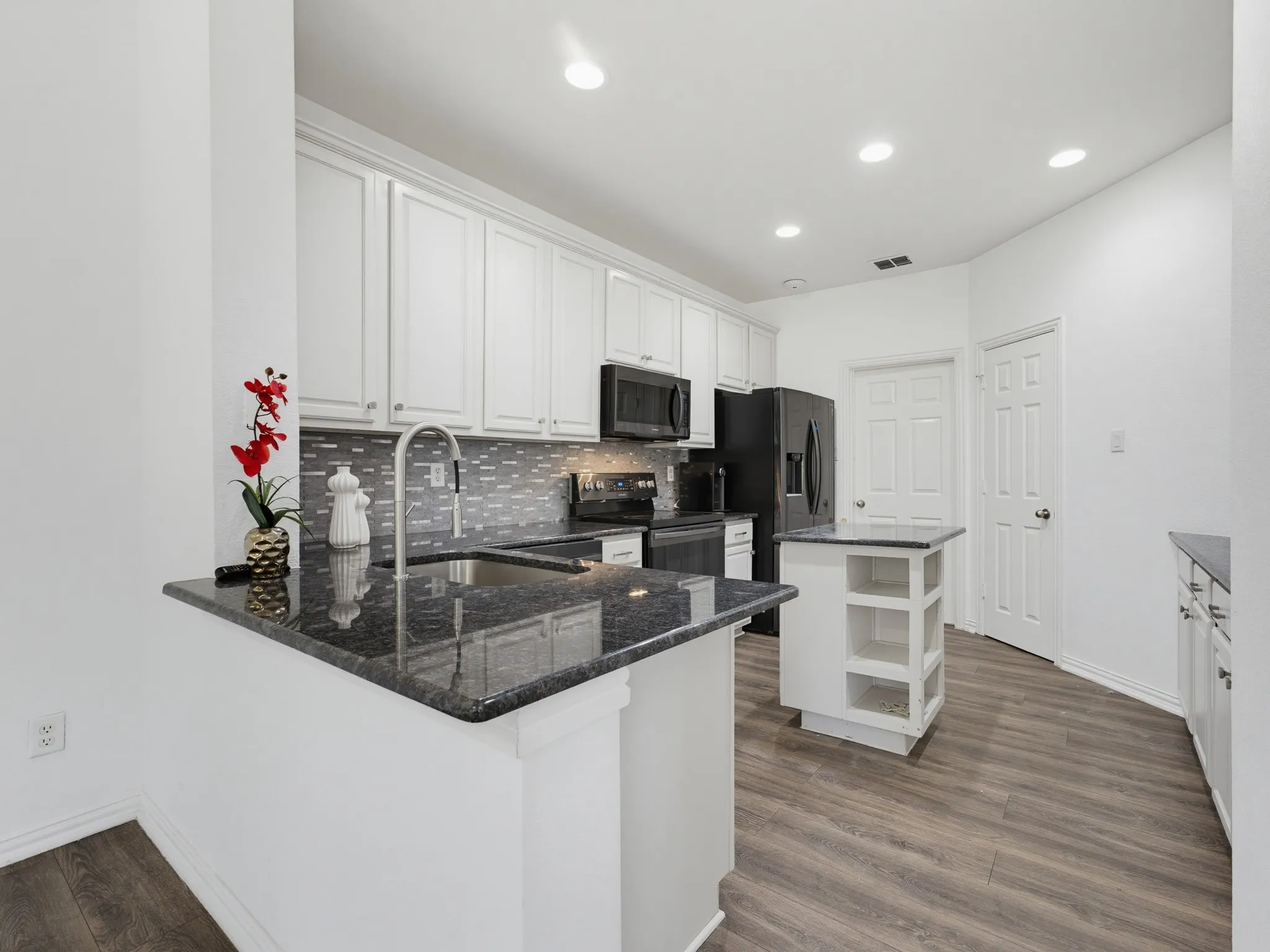 Kitchen featuring dark countertops, white cabinetry, dark appliances, wood-finish flooring, and recessed lighting