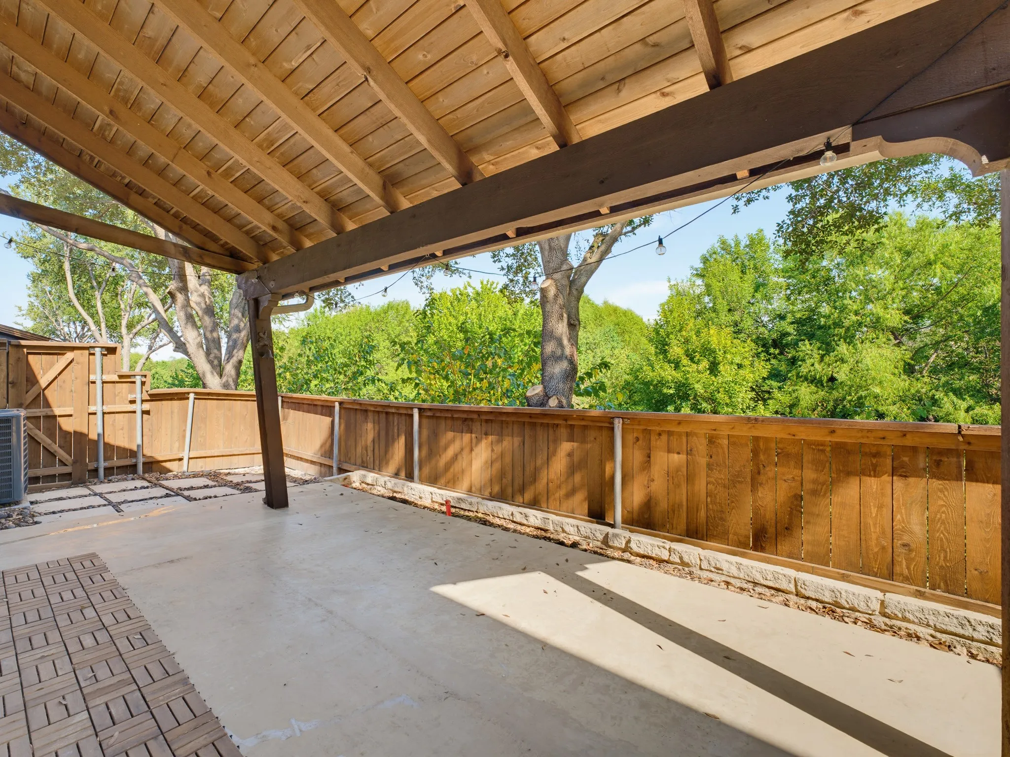 Covered patio featuring an exposed wood beam ceiling, concrete flooring, wood privacy fencing, and string lighting