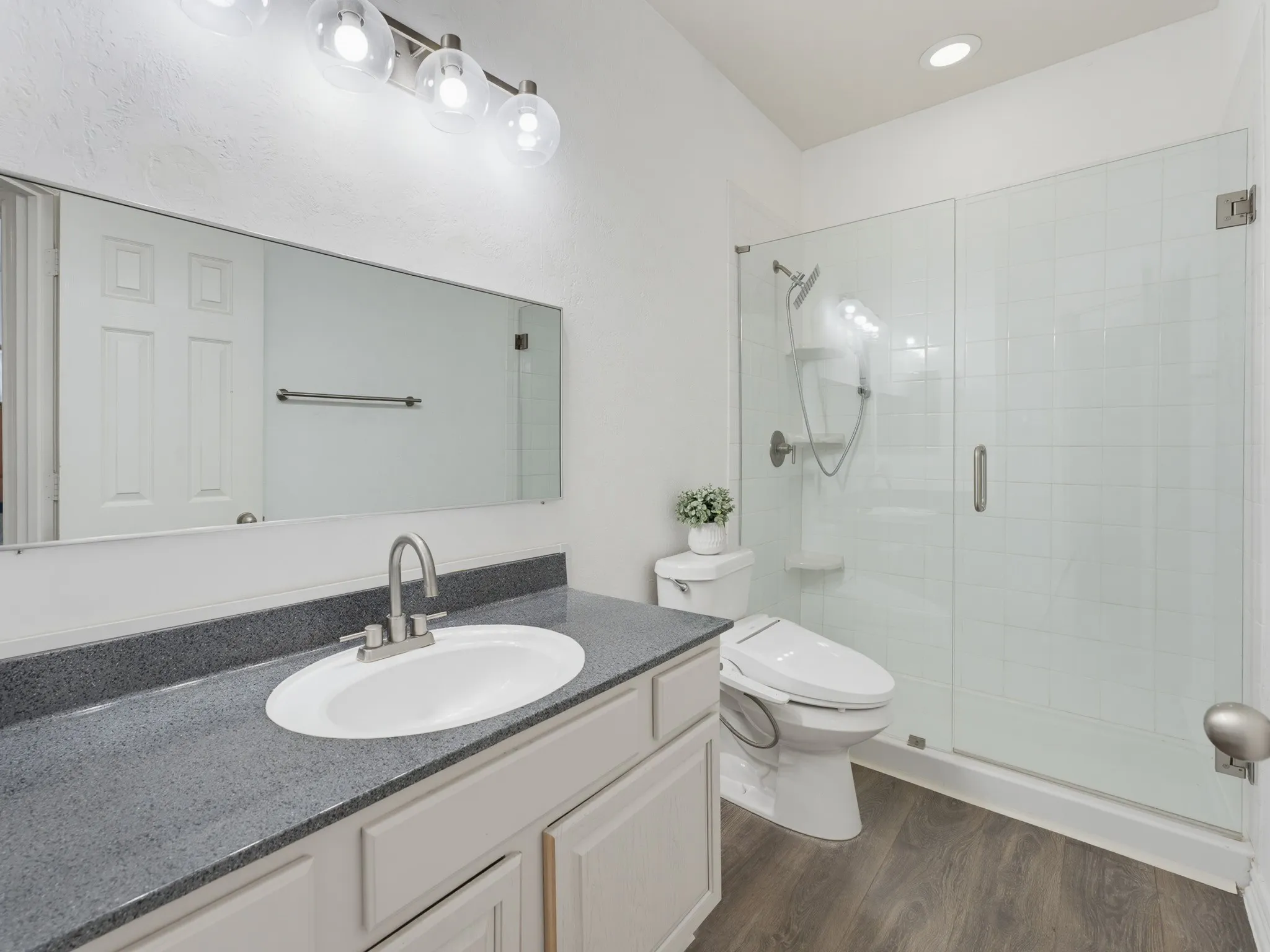 Bathroom featuring a single vanity with a gray countertop, an undermount sink, and a glass-enclosed shower