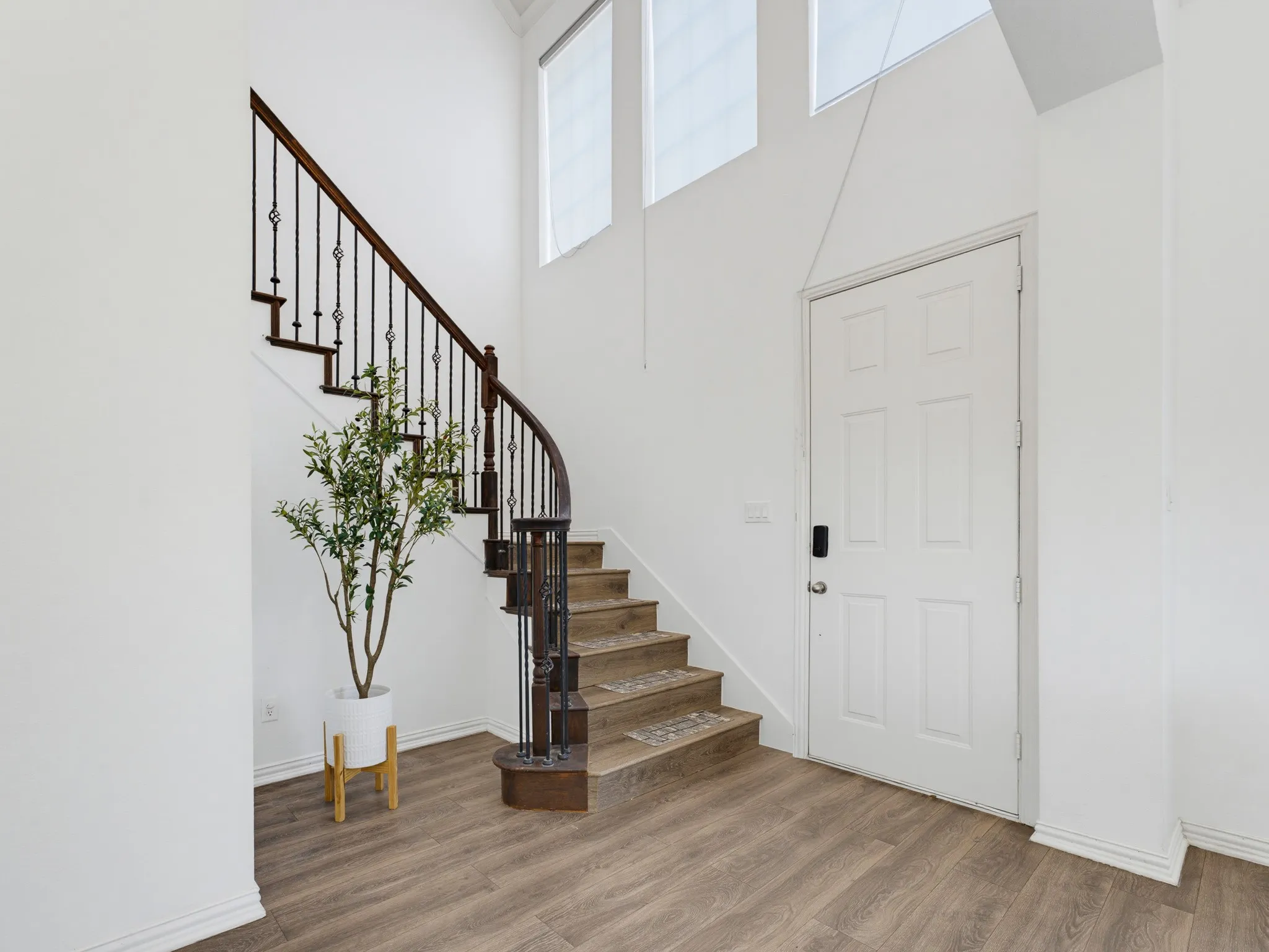 Two-story entry featuring wood-finish flooring, a winding staircase with wrought iron balusters, and transom windows