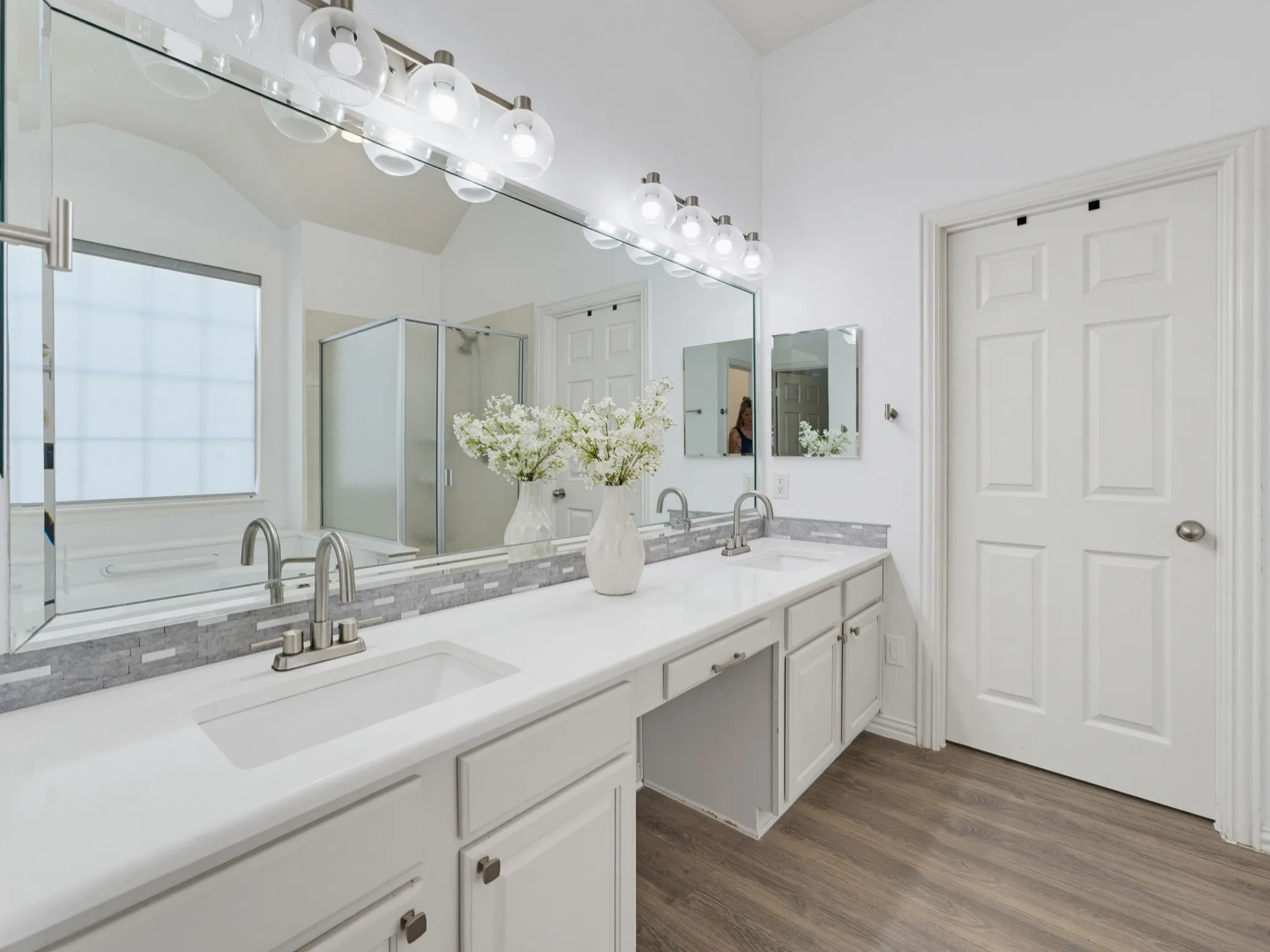 Dual vanity with white cabinetry and integrated sinks, complemented by a mosaic tile backsplash and wood-finish flooring