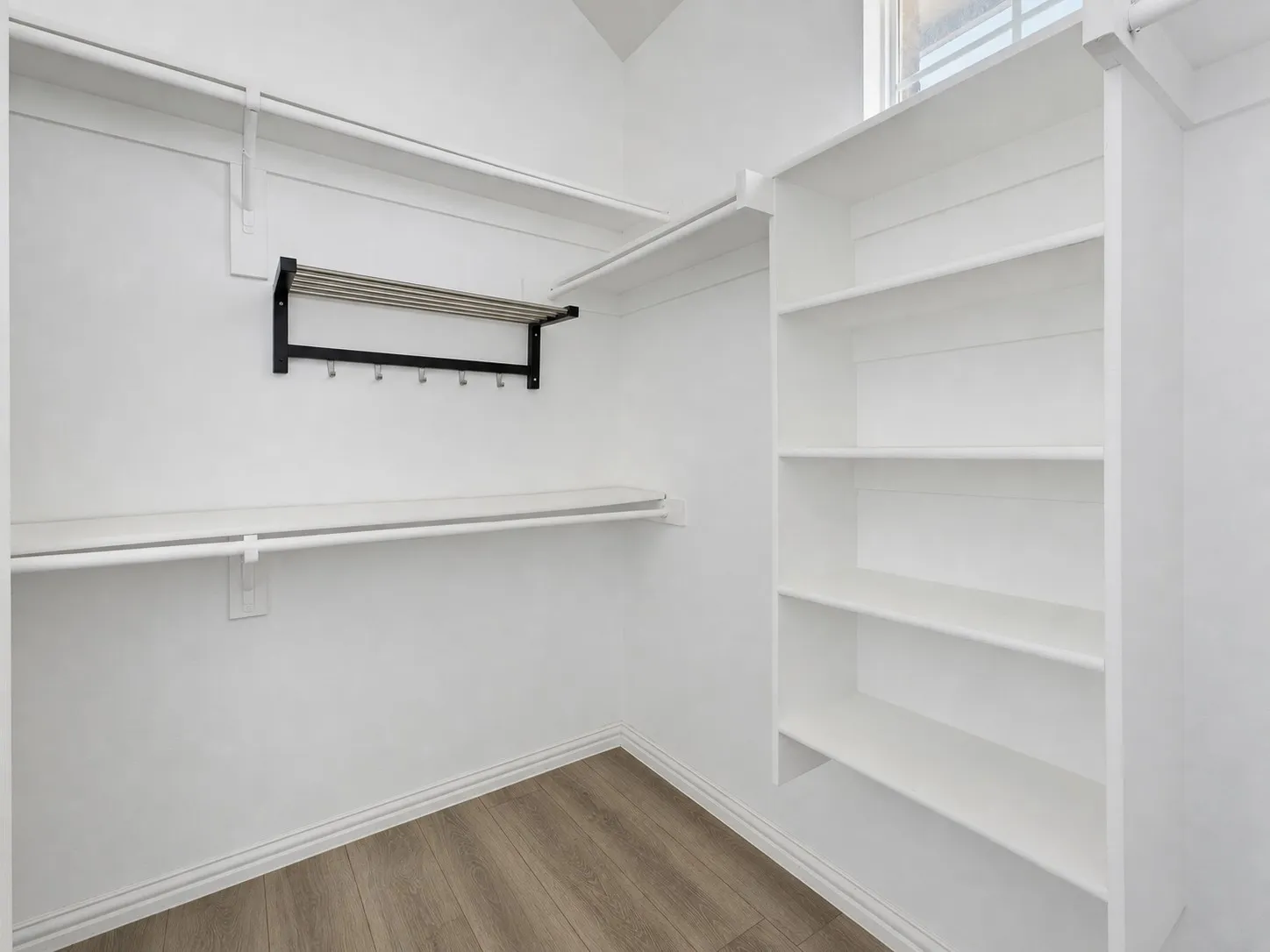 Built-in shelving, hanging rods, and a wall-mounted rack with hooks complement the wood-finish flooring