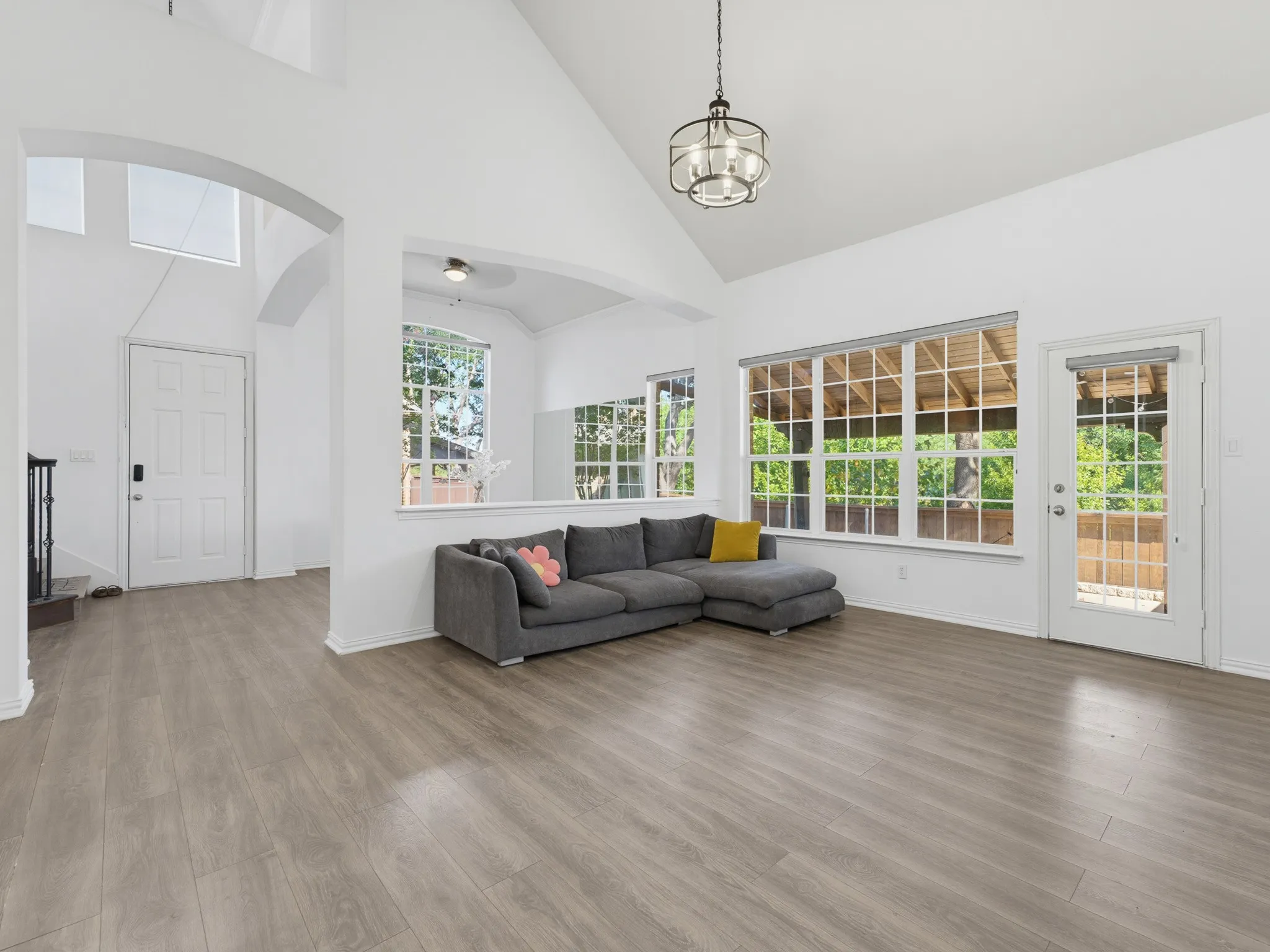 Vaulted ceilings, a decorative chandelier, ample natural light through large windows, wood-finish flooring, and a glass-paneled door