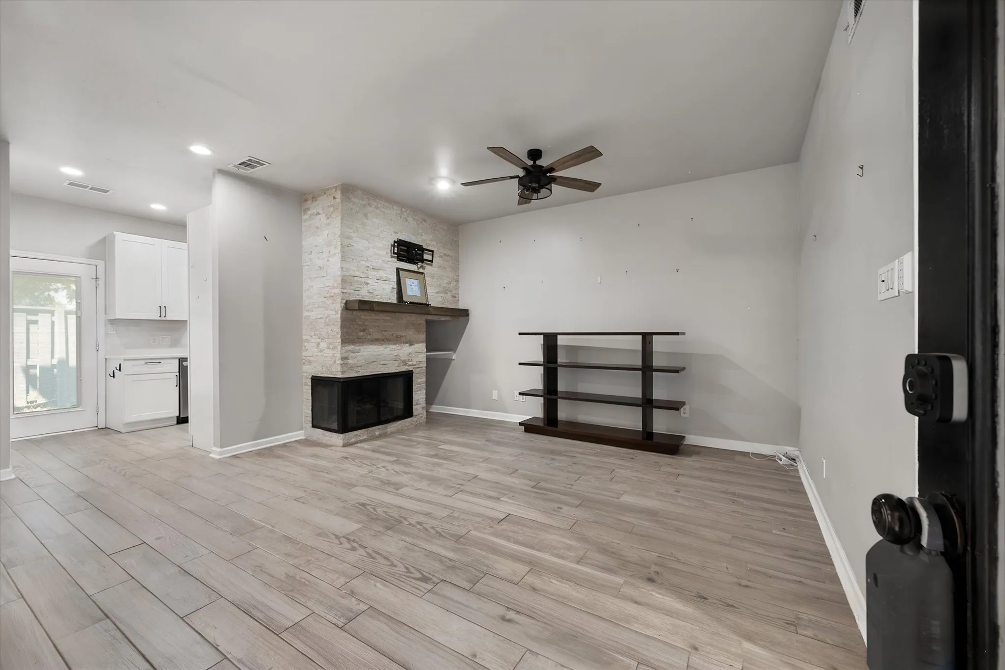 Living area featuring light wood-finish flooring, a stone-clad fireplace with a wood mantle, a ceiling fan with integrated lighting, recessed lighting, and a white cabinet with a stainless steel sink