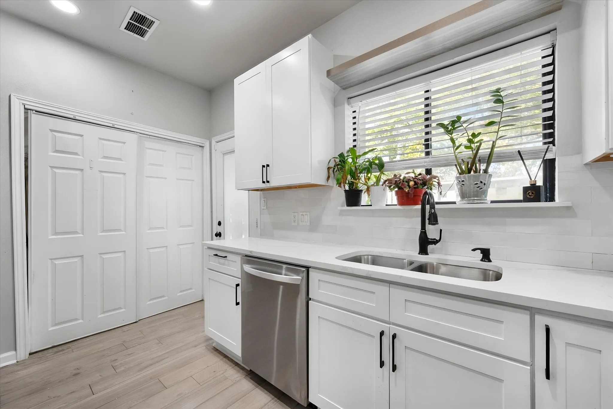 White shaker-style cabinetry with matte black hardware, stainless steel double basin sink, white stone countertops, and a white subway tile backsplash