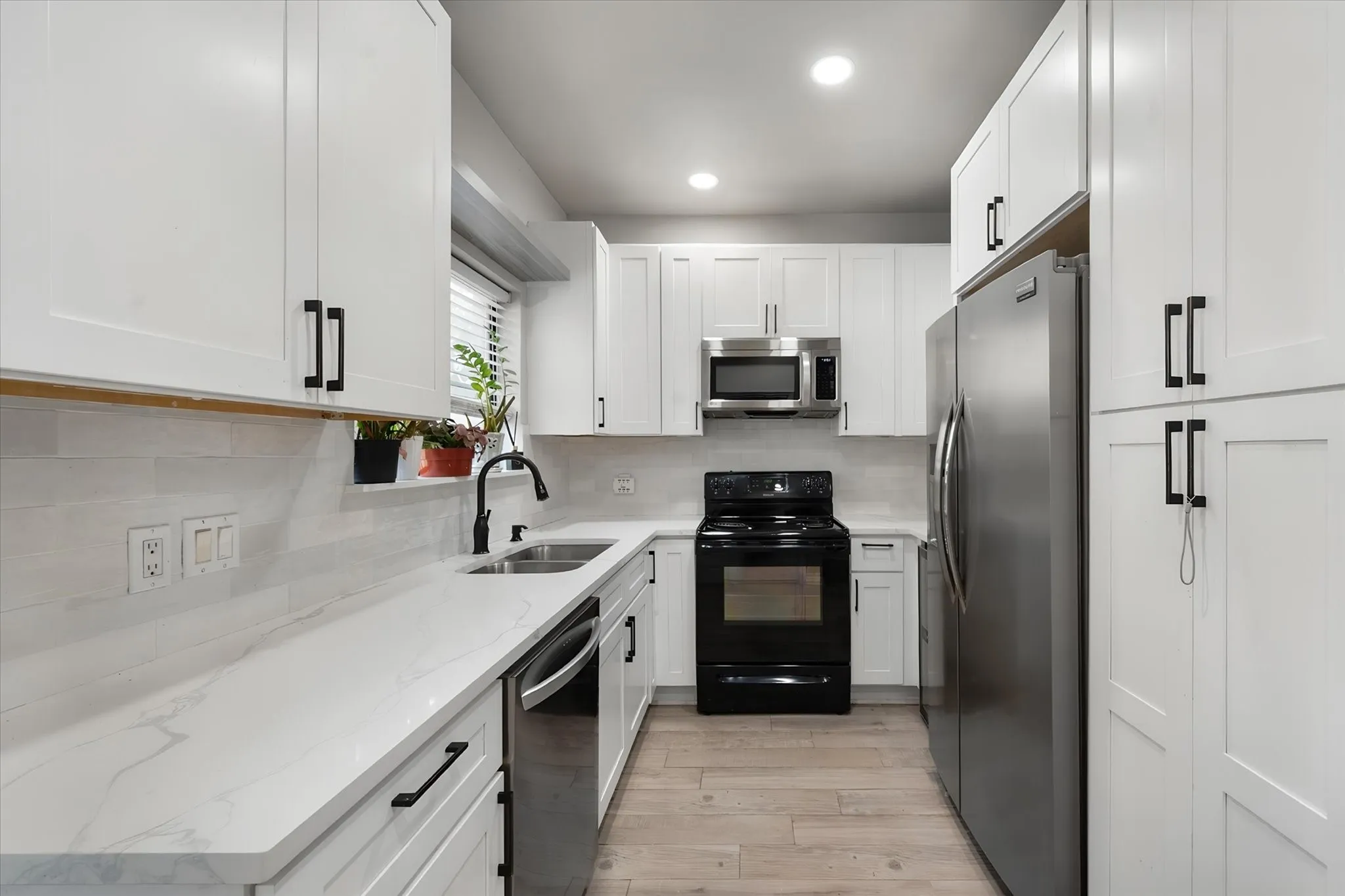 Updated kitchen featuring white shaker cabinetry, stainless steel appliances, light-toned wood-finish flooring, white countertops, and a white subway tile backsplash