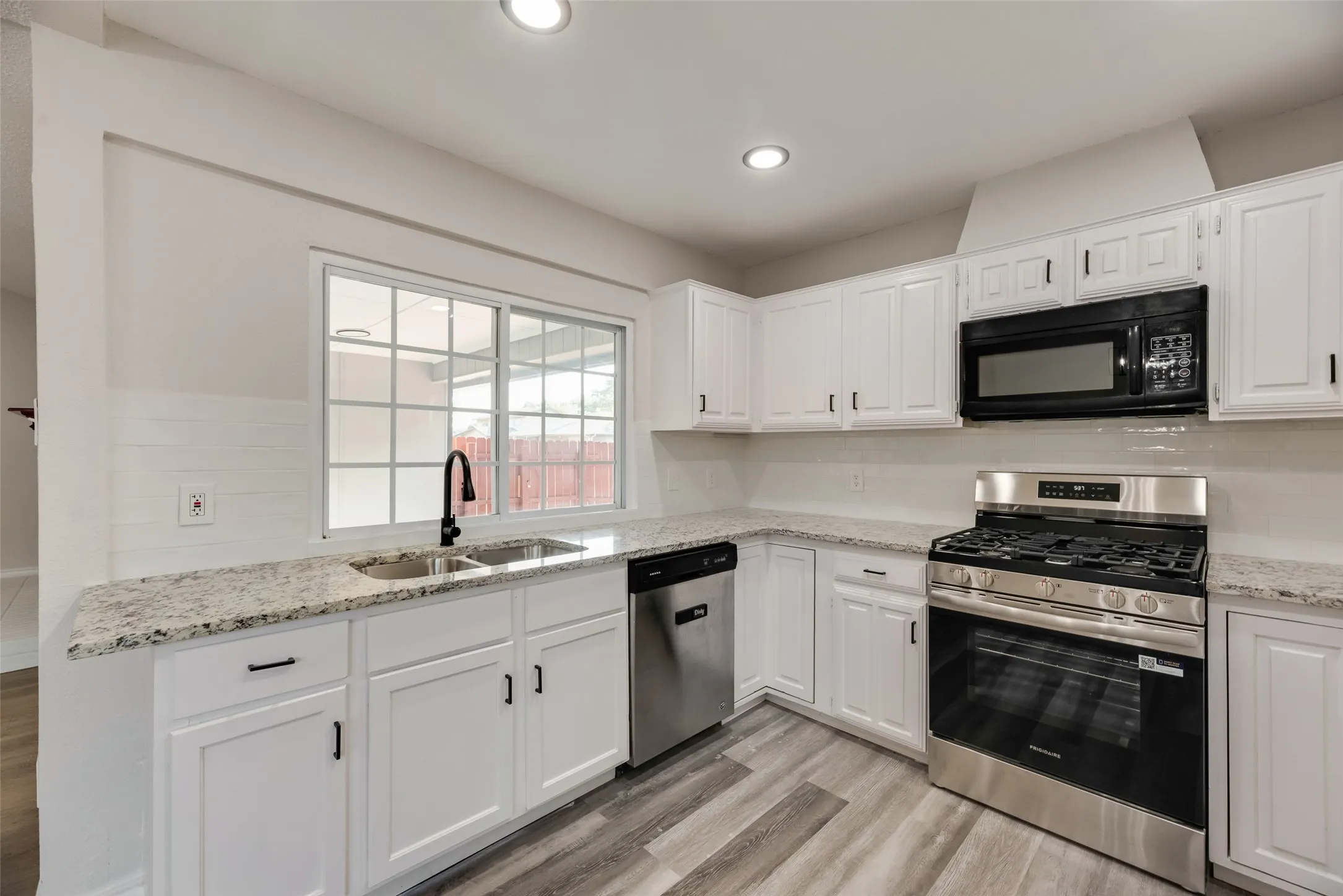 Modern kitchen featuring white cabinetry, light-toned countertops, wood-finish flooring, a stainless steel range, and a black microwave
