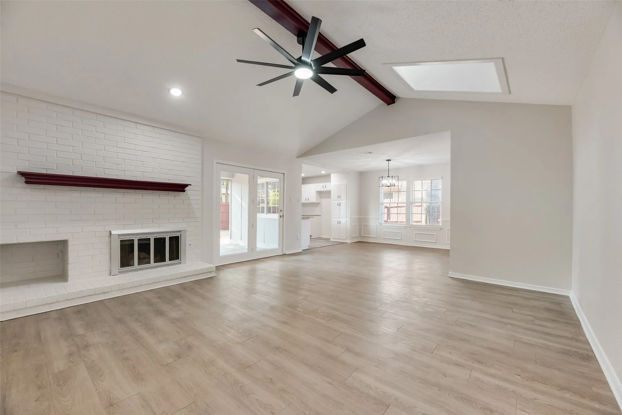 Vaulted ceiling with exposed beam, wood-finish flooring, white brick fireplace, modern ceiling fan, and double patio doors