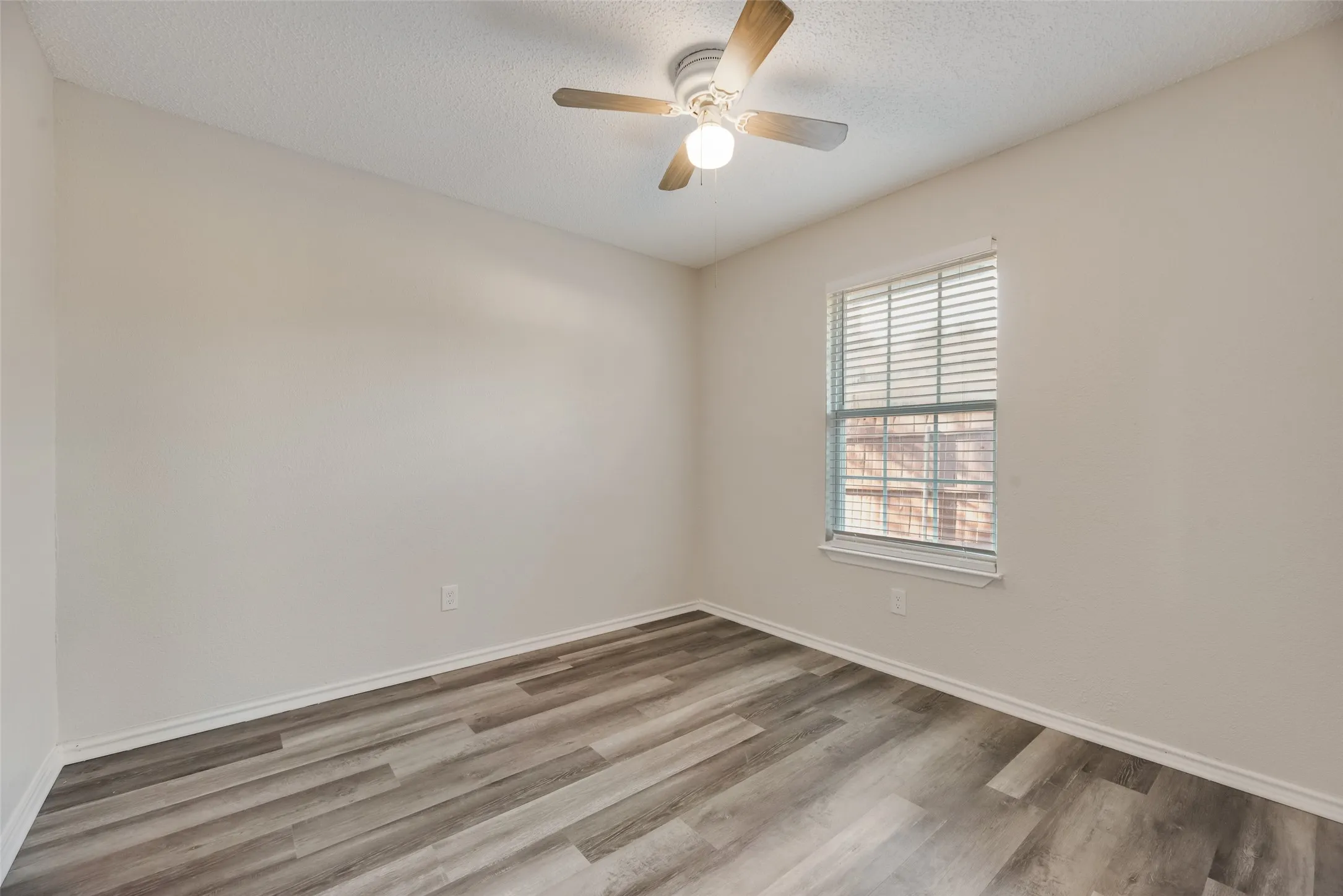 Wood-finish flooring, neutral wall paint, window with blinds, ceiling fan with integrated lighting