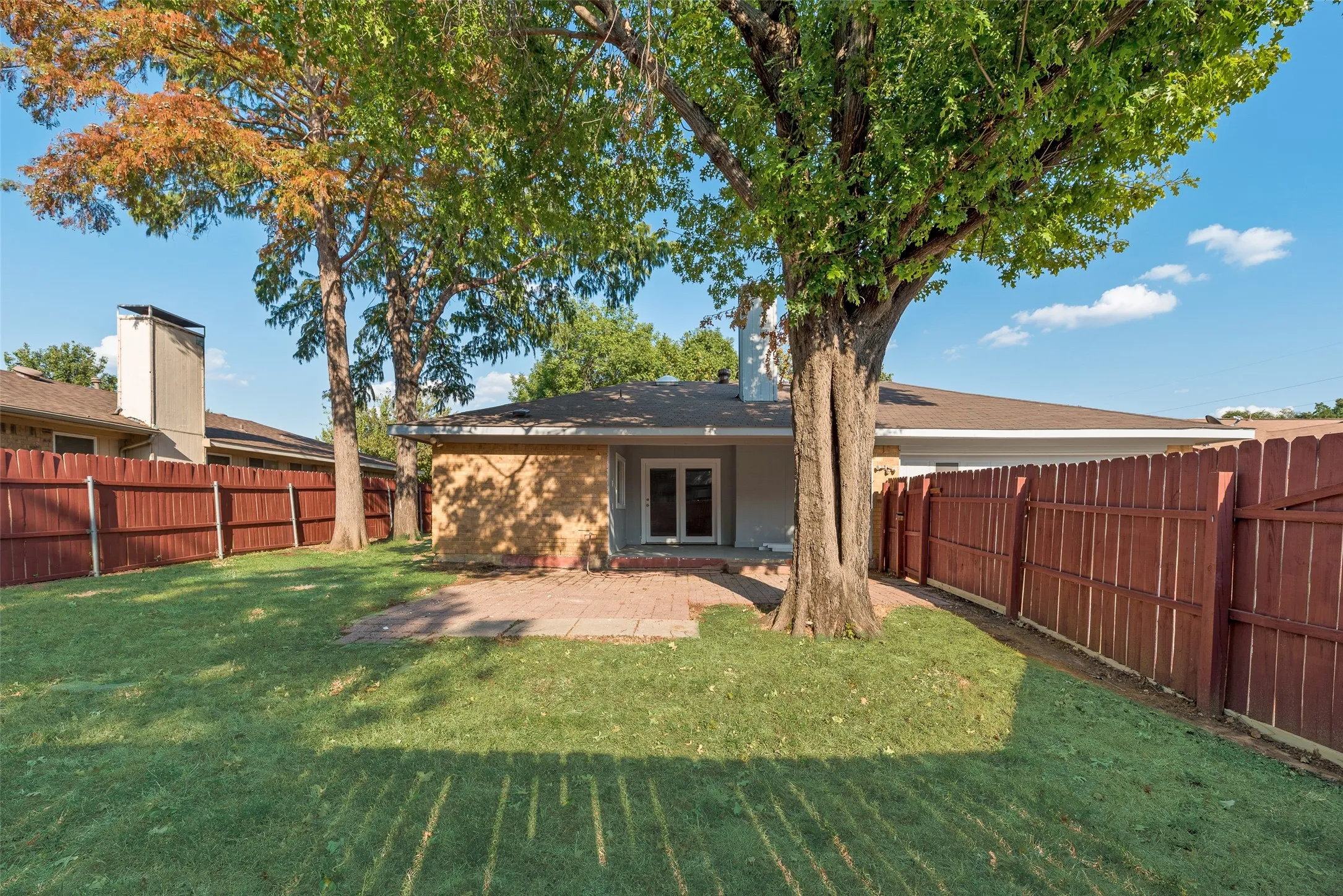 Fenced backyard featuring mature trees, a paver patio, brick and stucco exterior, and double glass doors