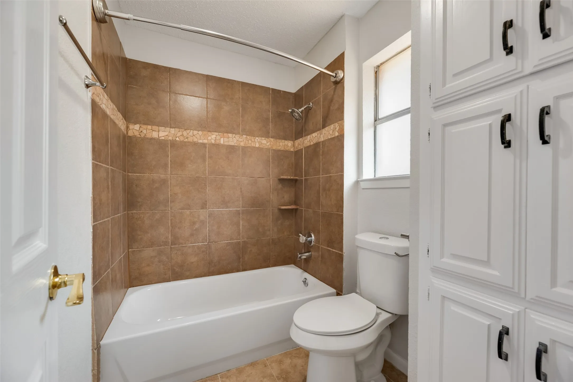 Bathtub with tiled surround featuring a decorative mosaic accent and built-in shelving