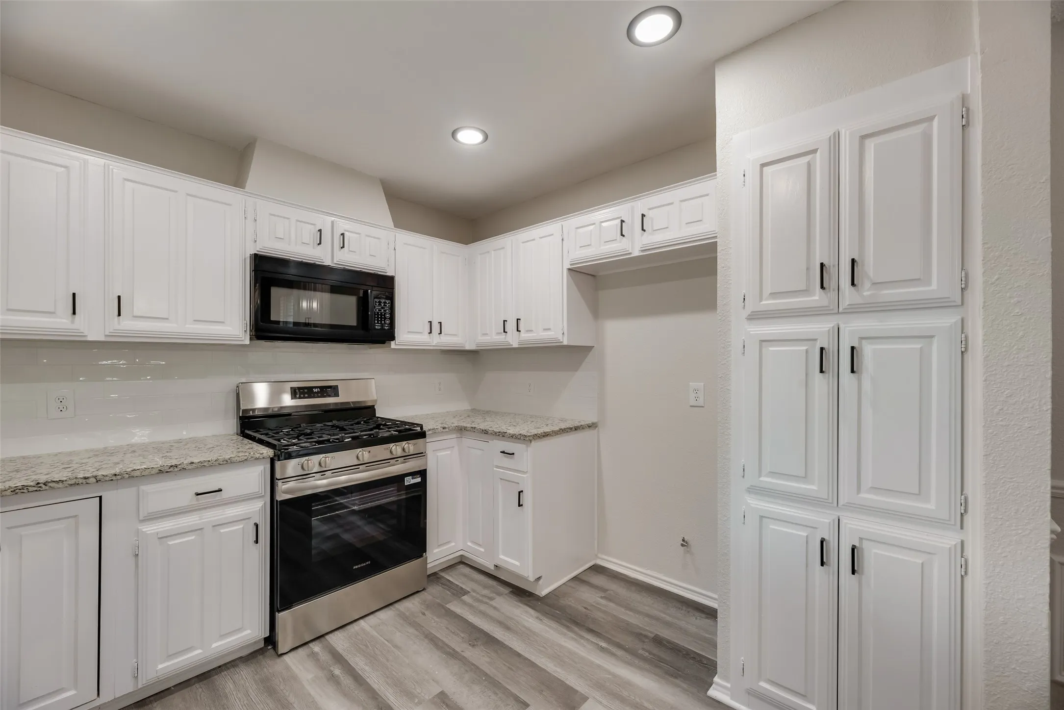 White shaker-style cabinetry, granite countertops, stainless steel range, built-in microwave, and wood-finish flooring