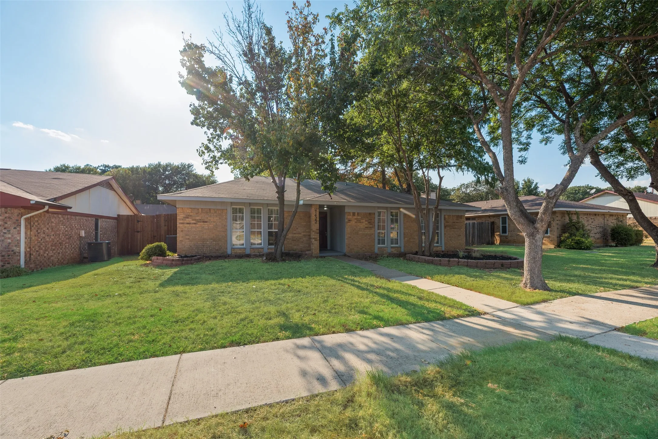 Brick exterior residence featuring a front yard, mature trees, and a concrete walkway