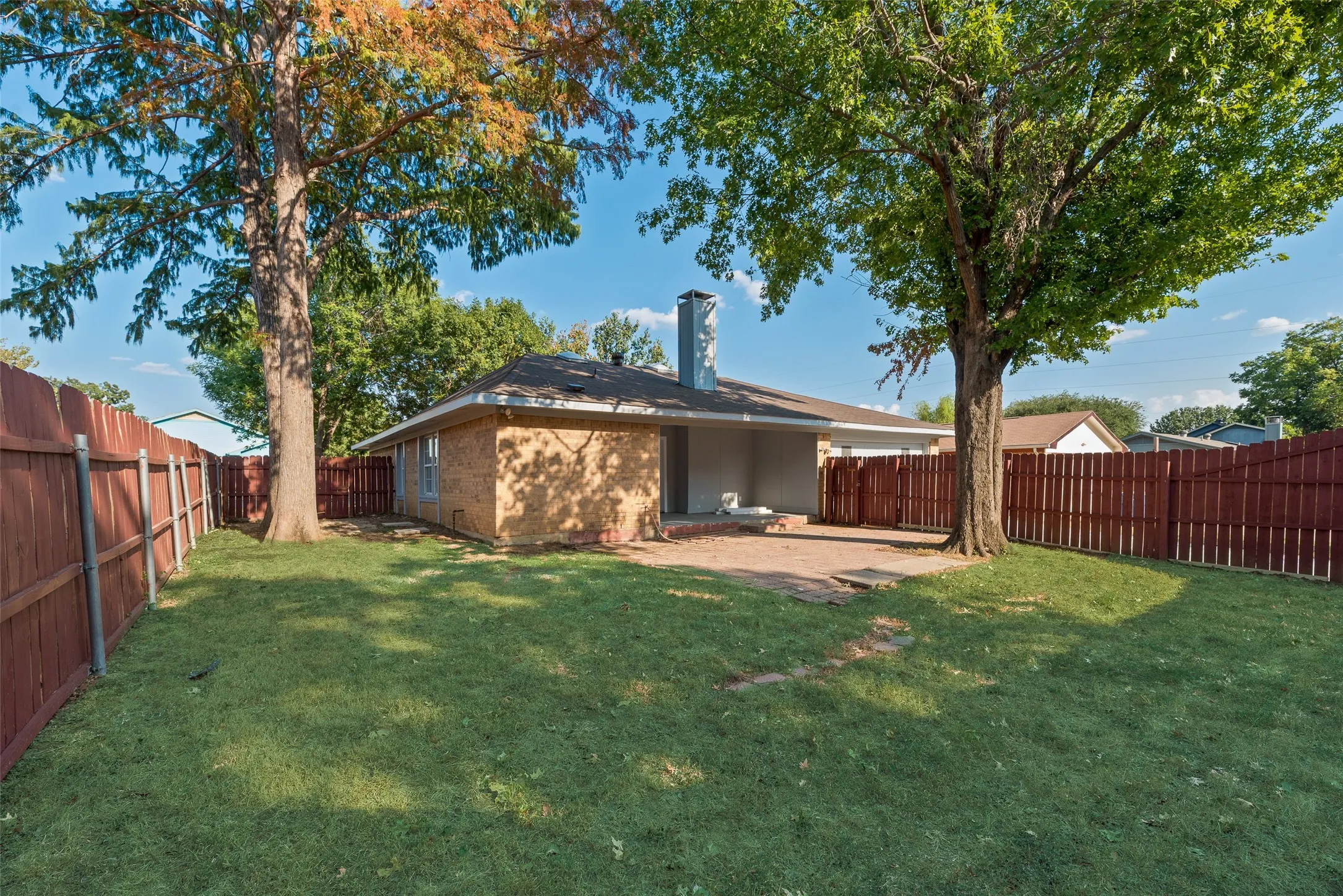 Manicured lawn with mature shade trees, full privacy fencing, and a paved patio area