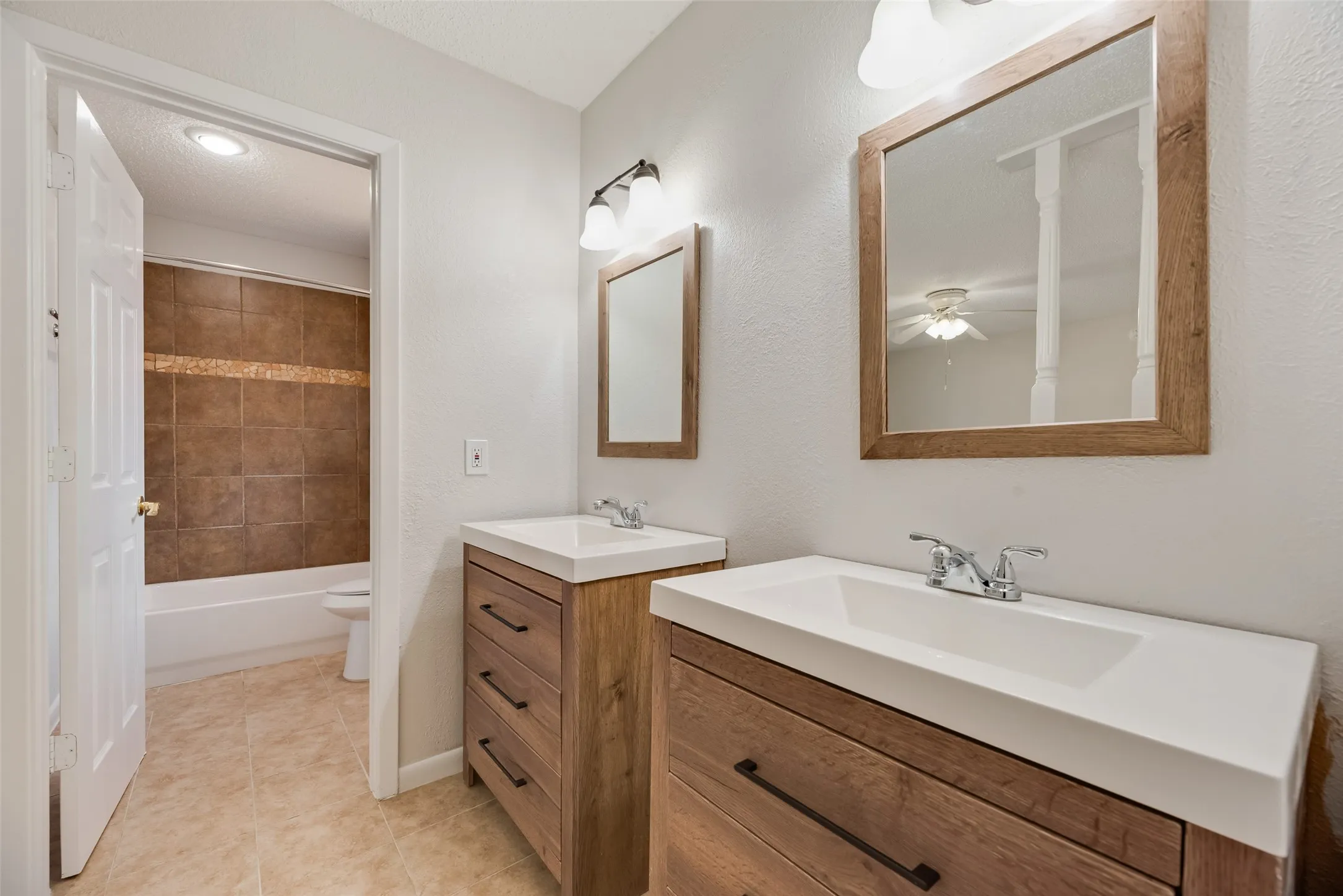 Dual vanities with wood-finish cabinetry, integrated sinks, and wall-mounted light fixtures