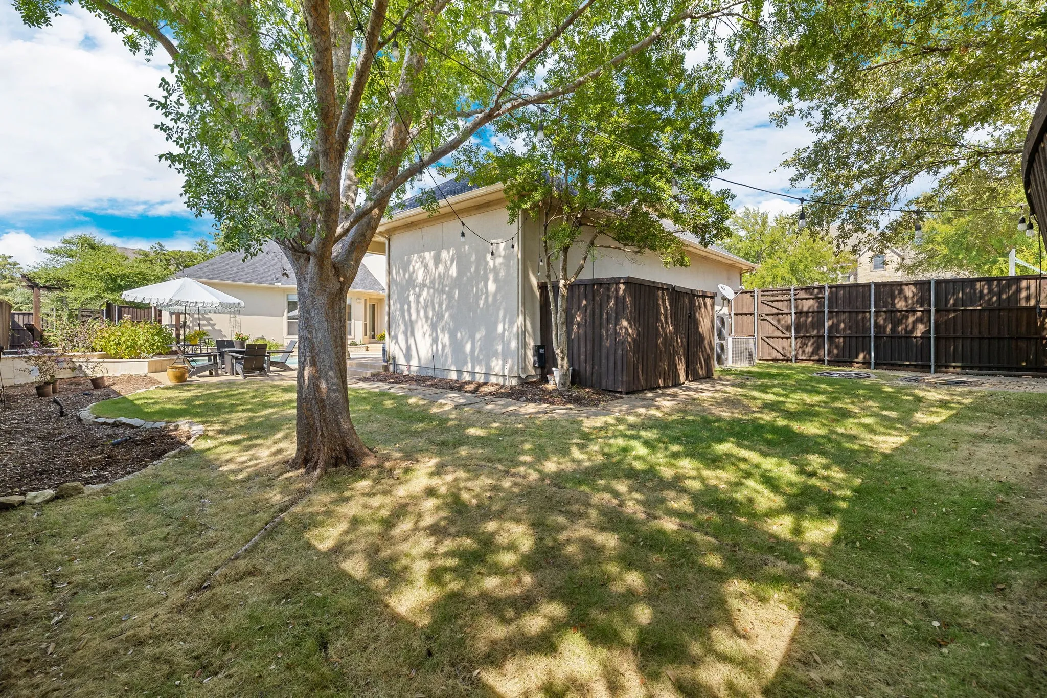Large grassy yard with shade trees and outdoor building that conveys.