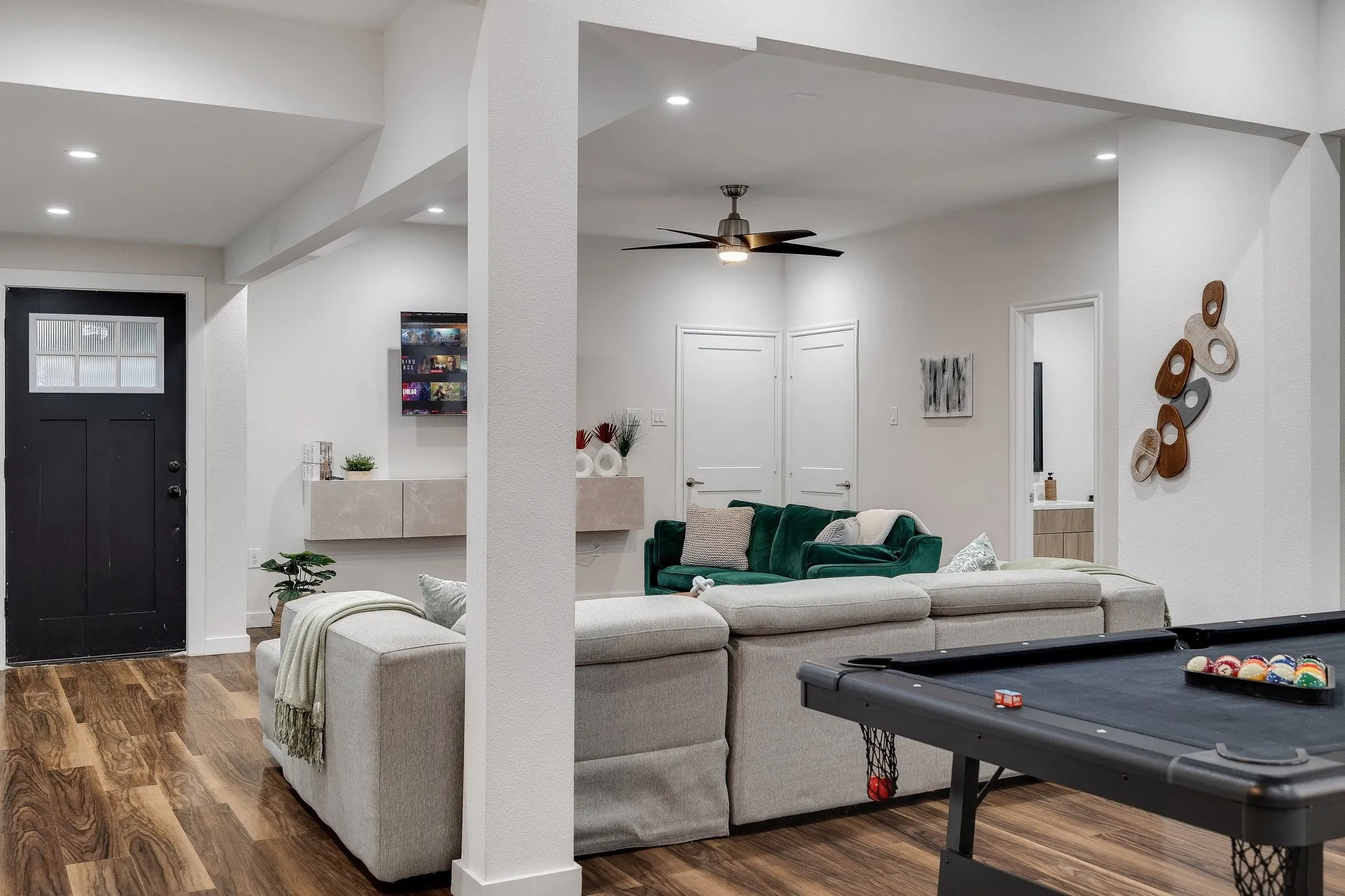 Wood-finish flooring, recessed lighting, ceiling fan, white walls, and a black paneled door with glass inserts