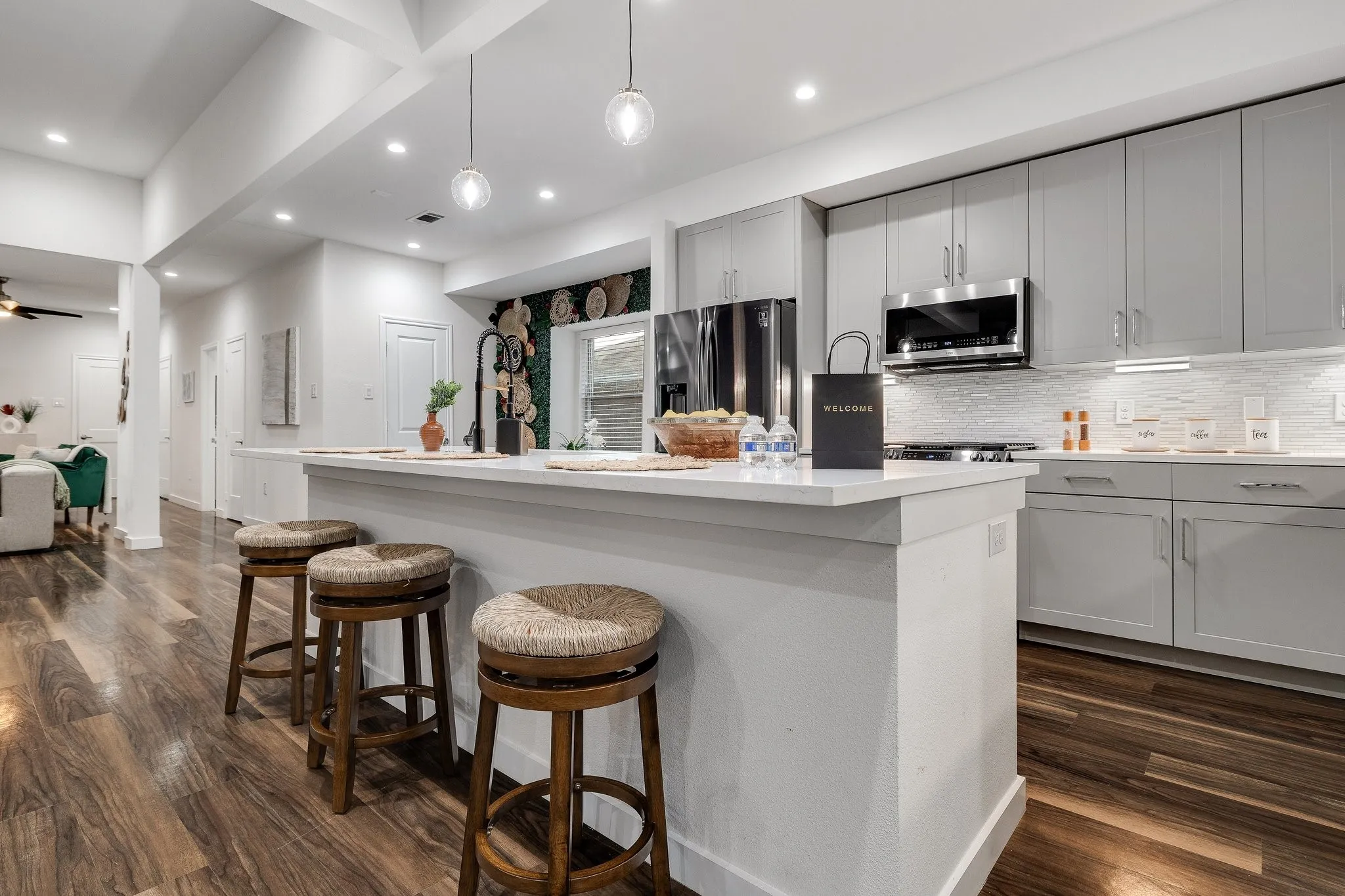 Open-concept kitchen featuring an island with counter seating, stainless steel appliances, light gray cabinetry, and wood-finish flooring