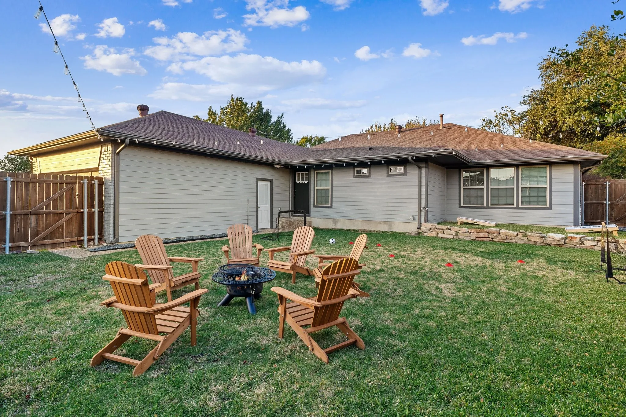 Spacious backyard retreat featuring a manicured lawn, mature landscaping, and multiple Adirondack seating arrangements ideal for outdoor entertaining