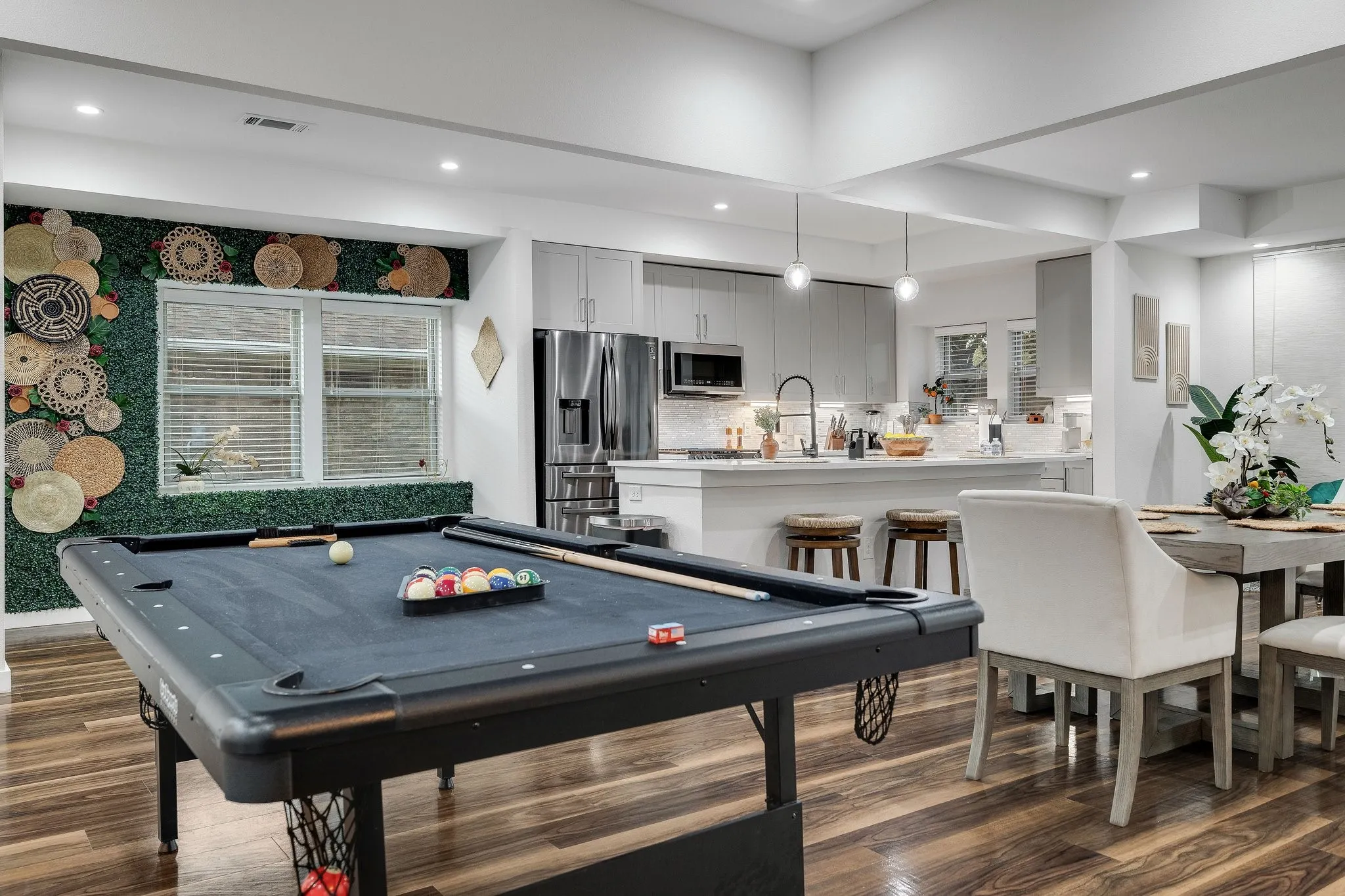 Open-concept living and entertaining space featuring a slate-finish pool table, custom cabinetry with stainless steel appliances, quartz countertops, wood-finish flooring throughout, and recessed ceiling lighting