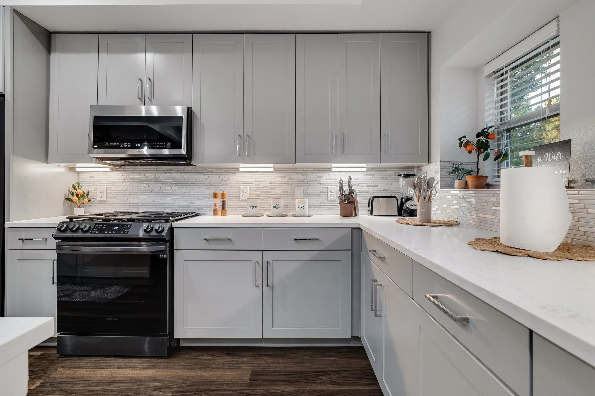 Kitchen featuring light gray cabinetry, stainless steel microwave, black range, white countertops, and wood-finish flooring