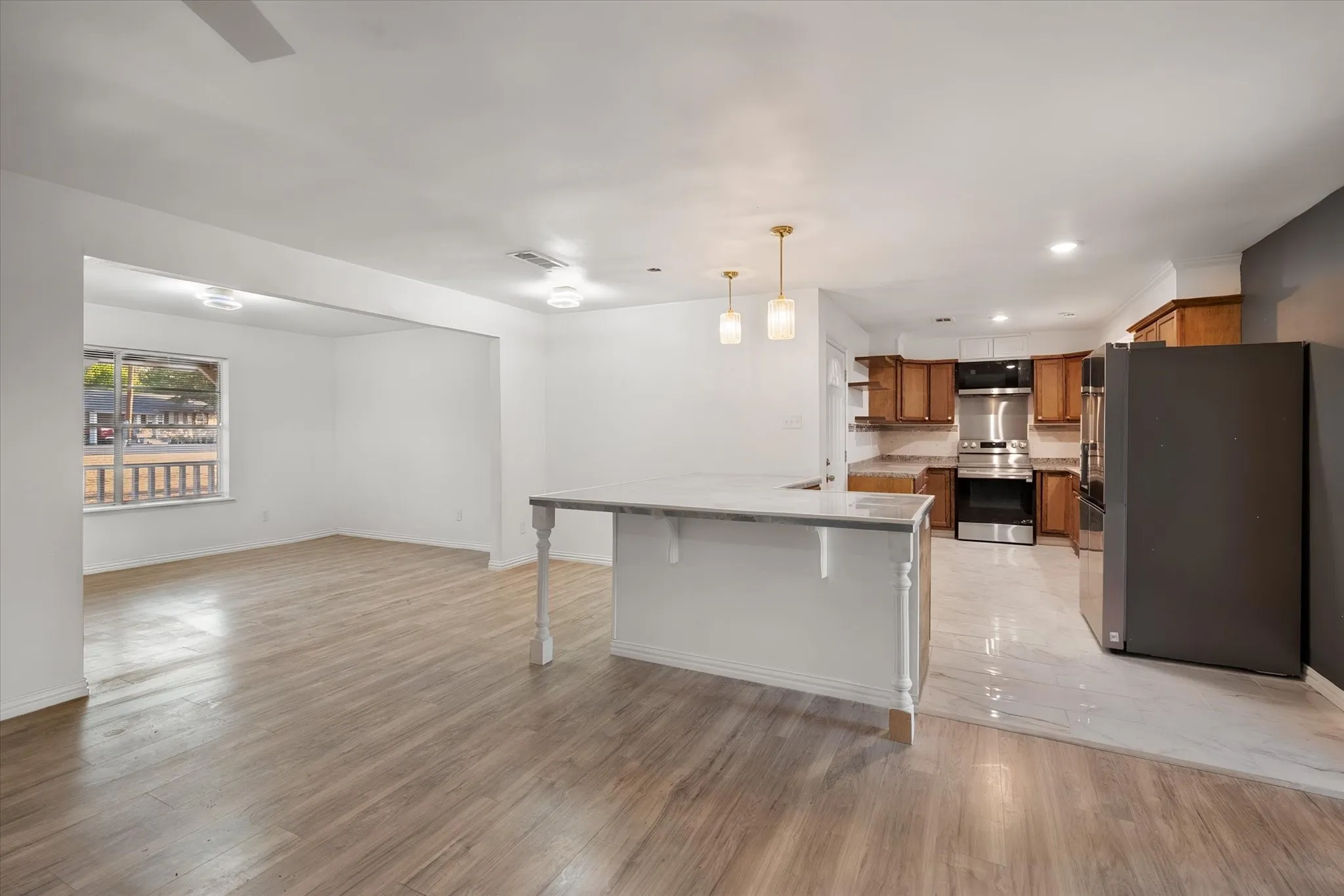 Open-concept living space with wood-finish flooring, a kitchen island with a stone countertop, pendant lighting, and stainless steel appliances