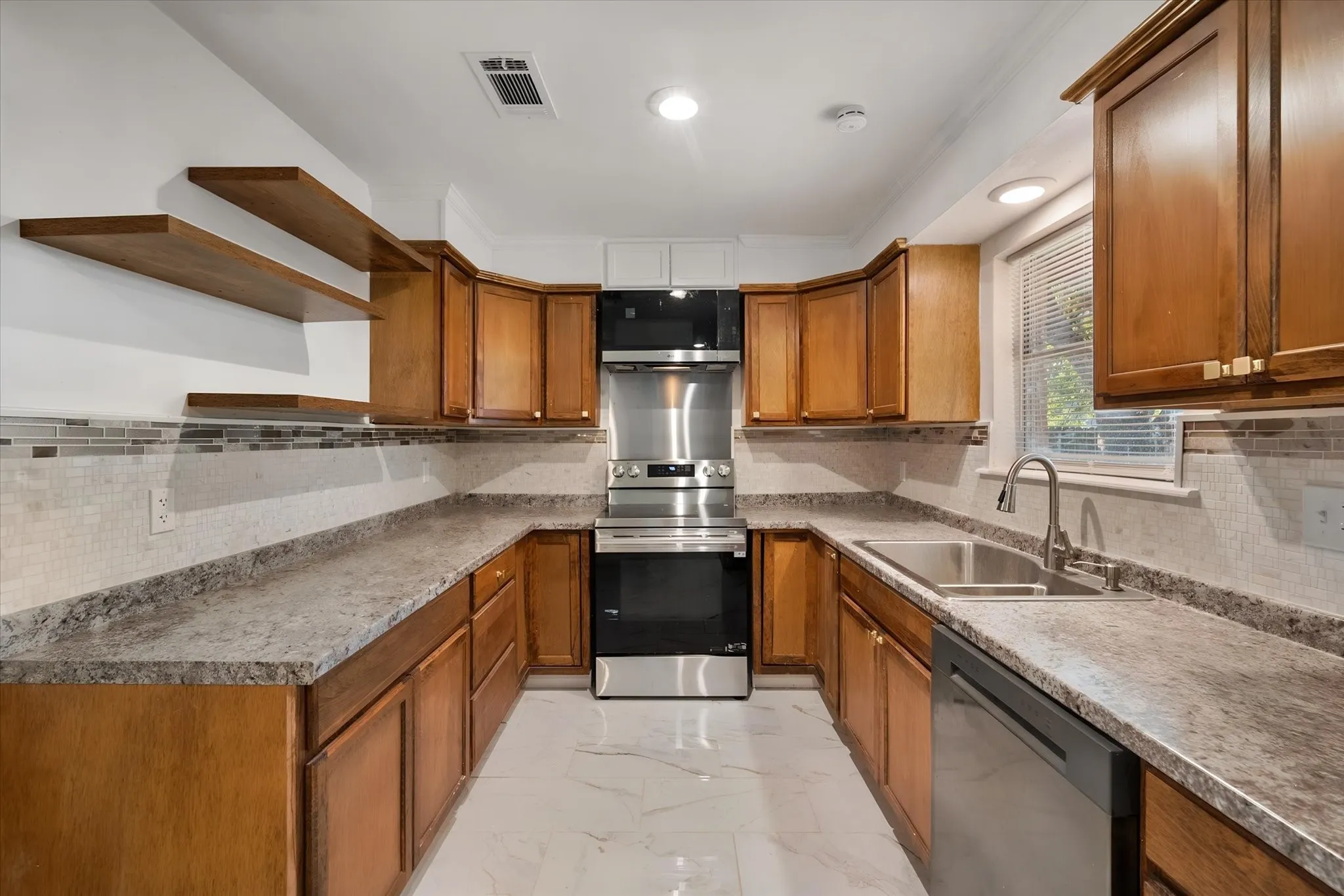 U-shaped kitchen with wood-finish cabinetry, stainless steel appliances, mosaic tile backsplash, and light-toned countertops