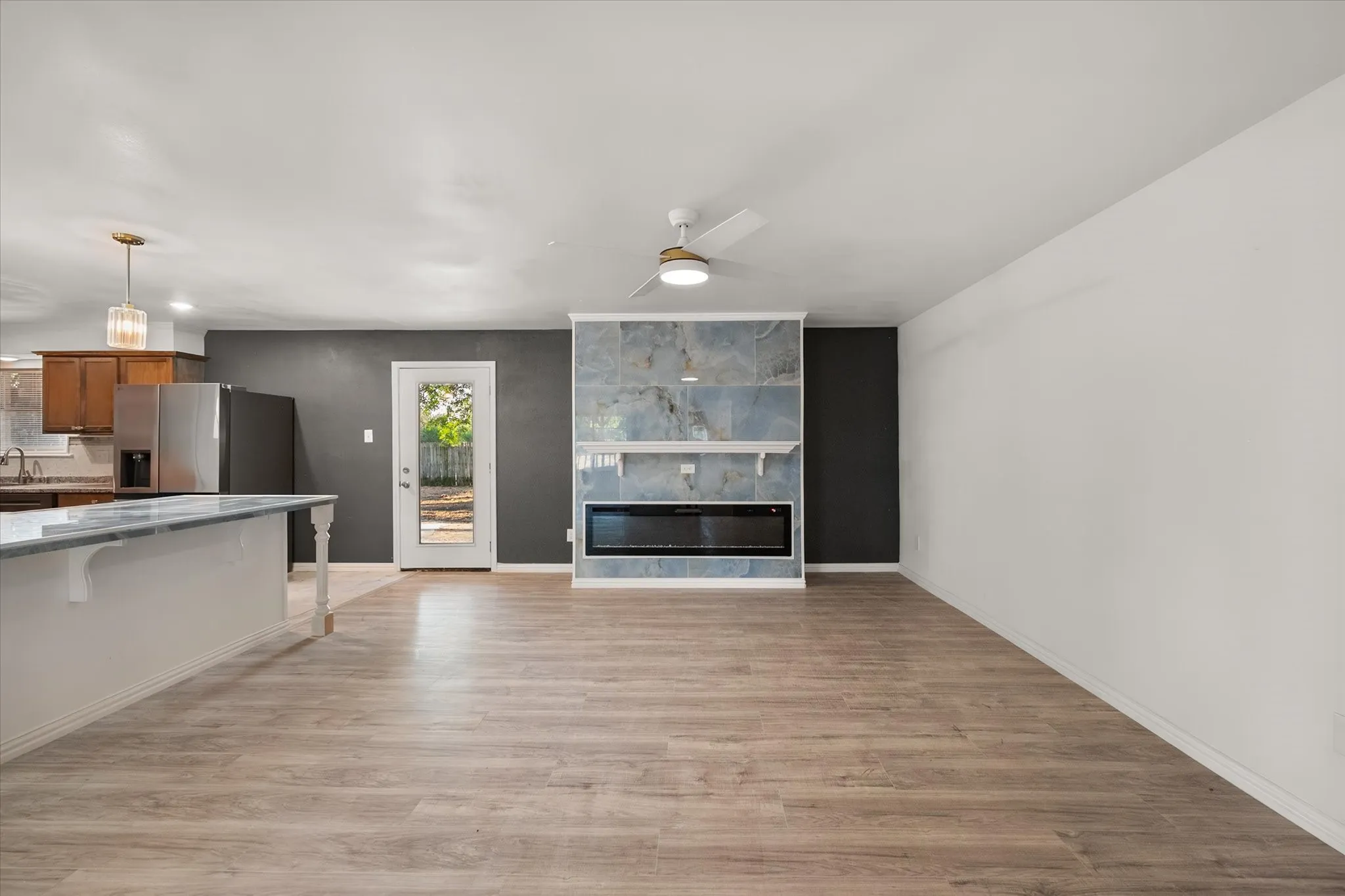 Open-concept living space with wood-finish flooring, a contemporary fireplace feature wall, recessed lighting, and a ceiling fan