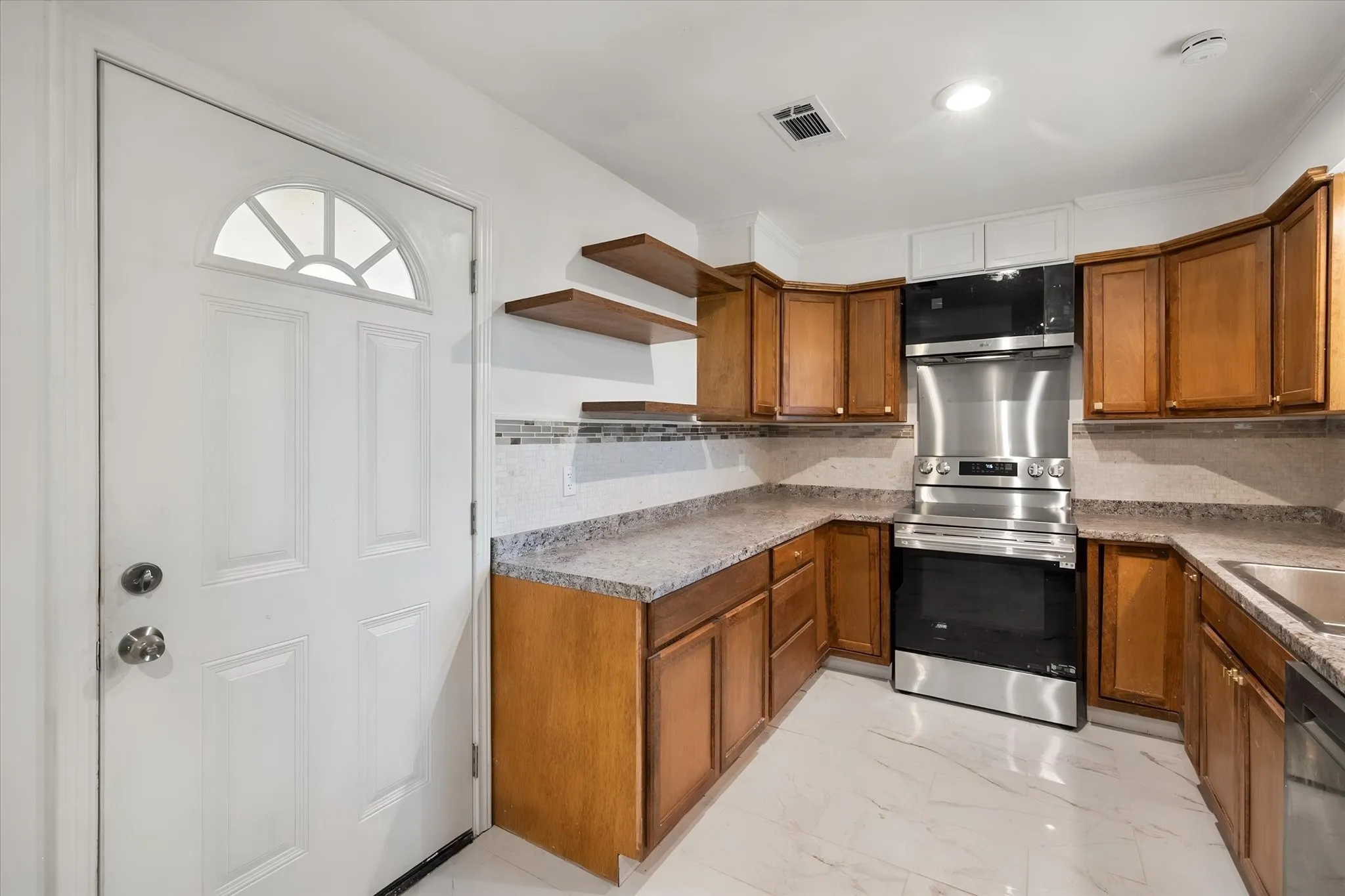 Entry door with a decorative transom, wood-finish cabinetry, stone-look countertops, subway tile backsplash, and stainless steel appliances