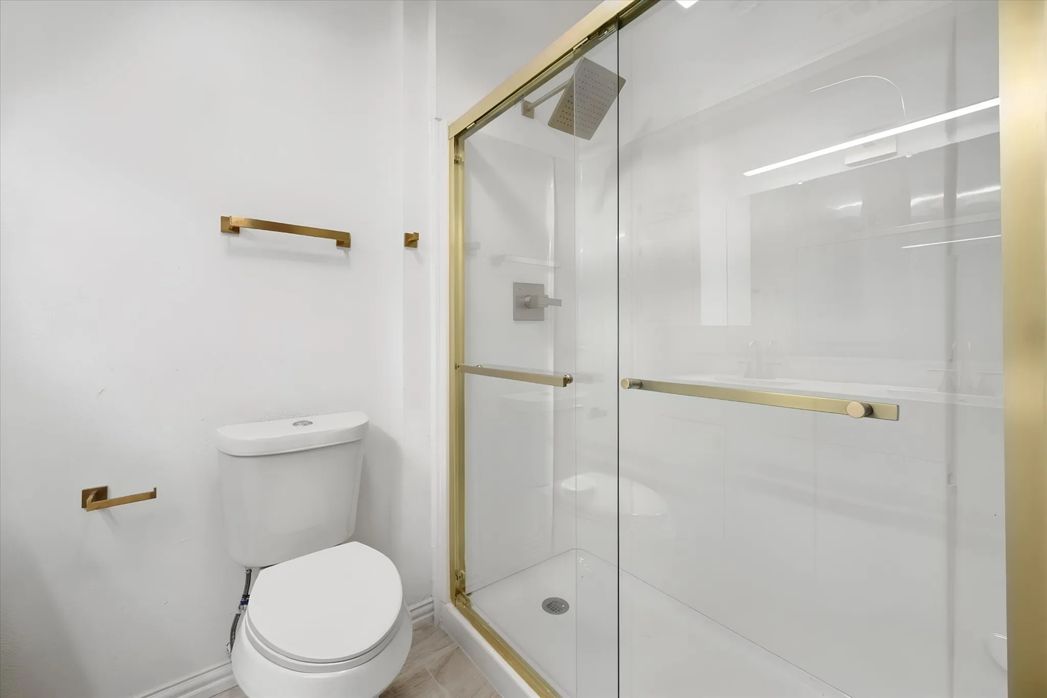 Shower with glass enclosure, brushed gold fixtures, and white tiled walls