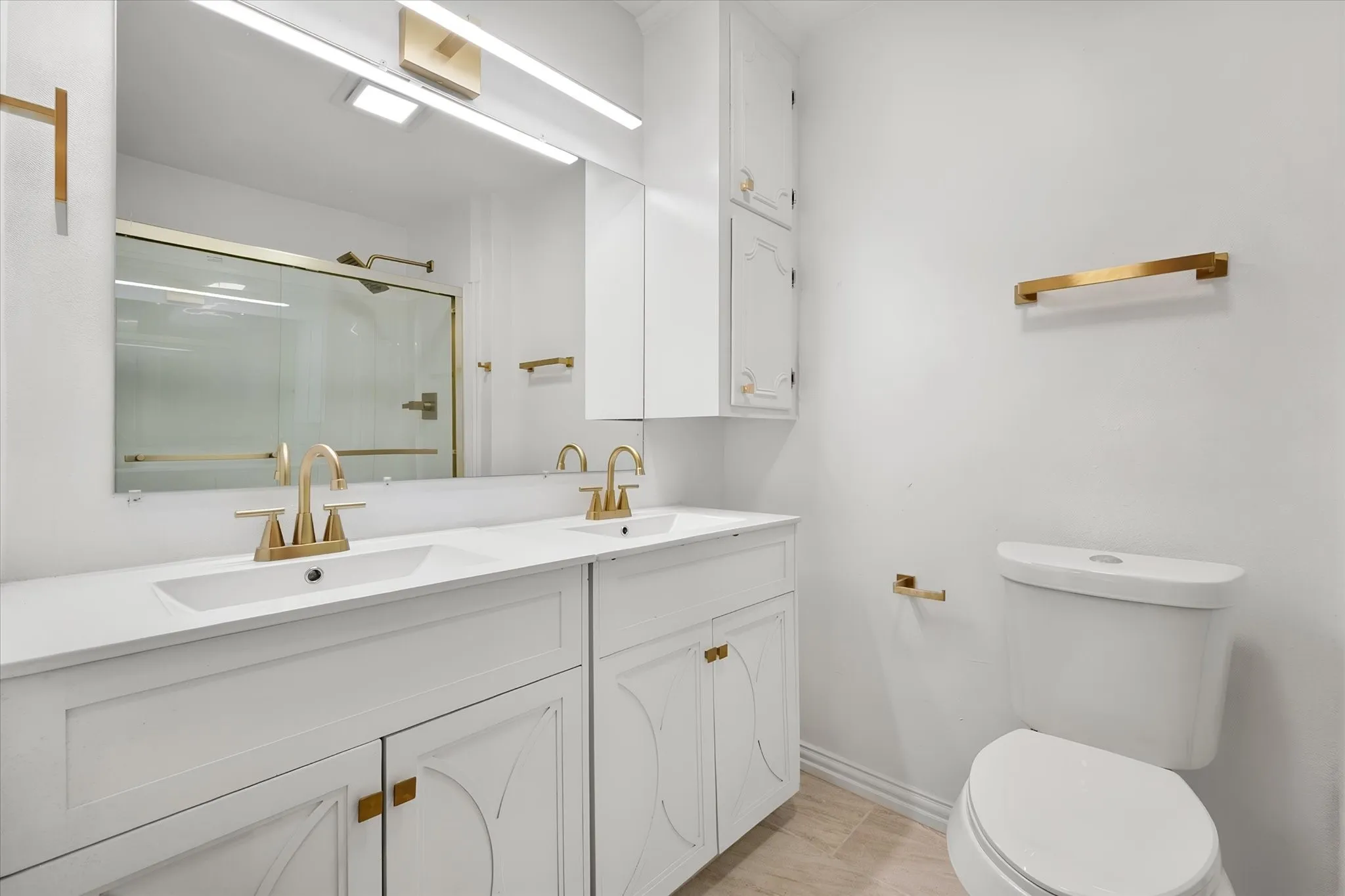 Dual vanity with integrated sinks, white cabinetry with gold-tone hardware, and an expansive wall mirror