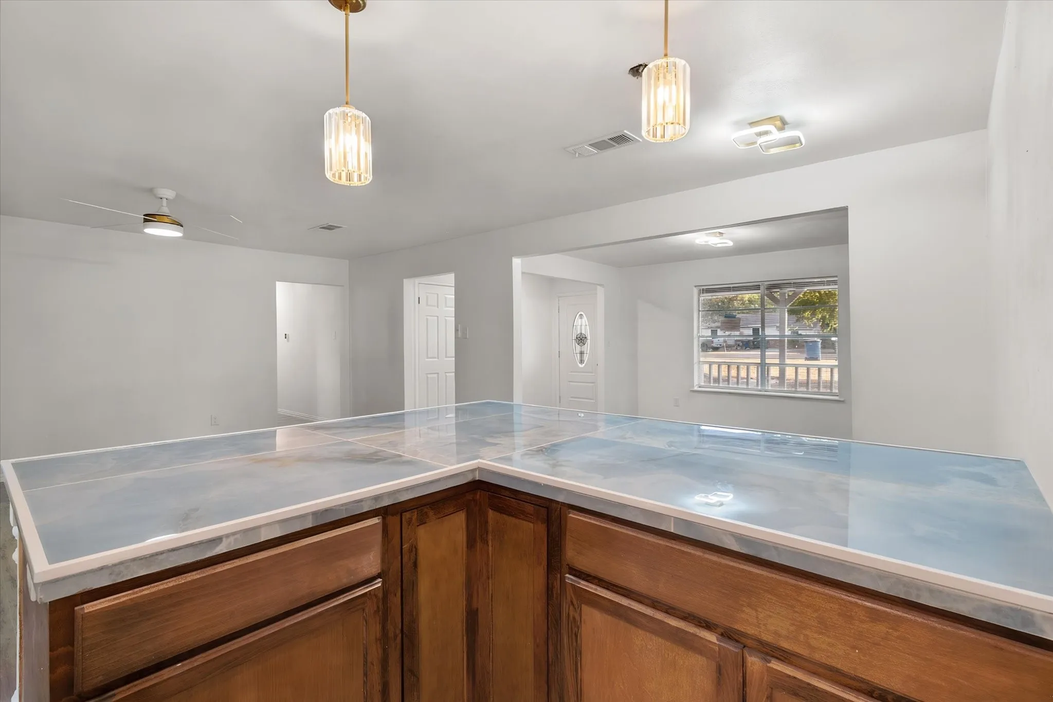 L-shaped counter featuring a patterned surface, wood-finish cabinetry, and overhead pendant lighting