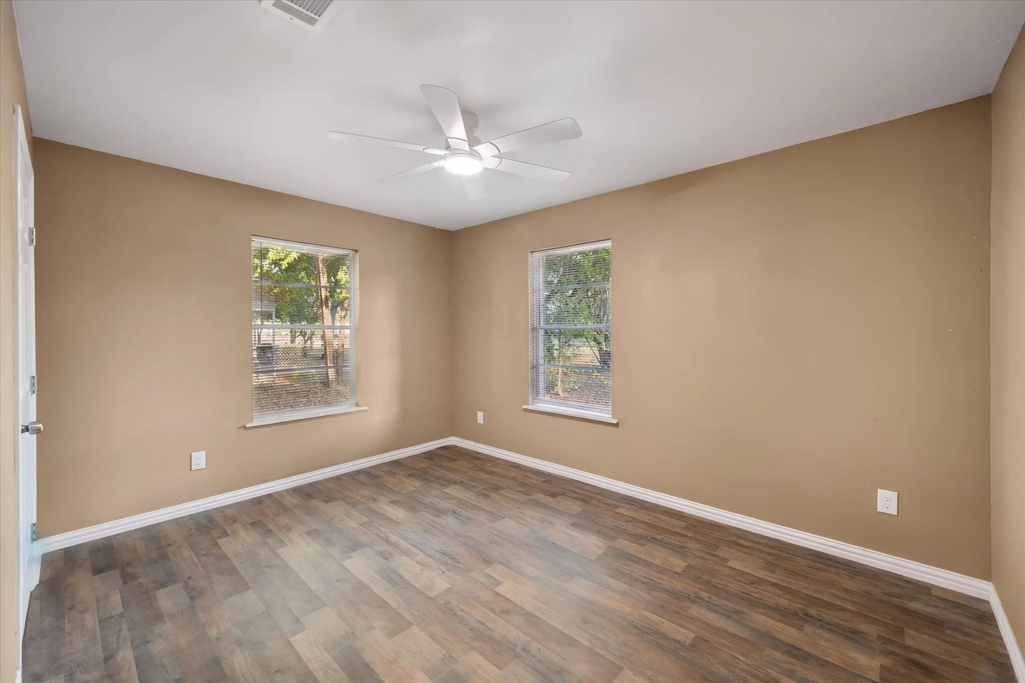 Room featuring wood-finish flooring, two windows, a ceiling fan with integrated lighting, and a neutral wall color