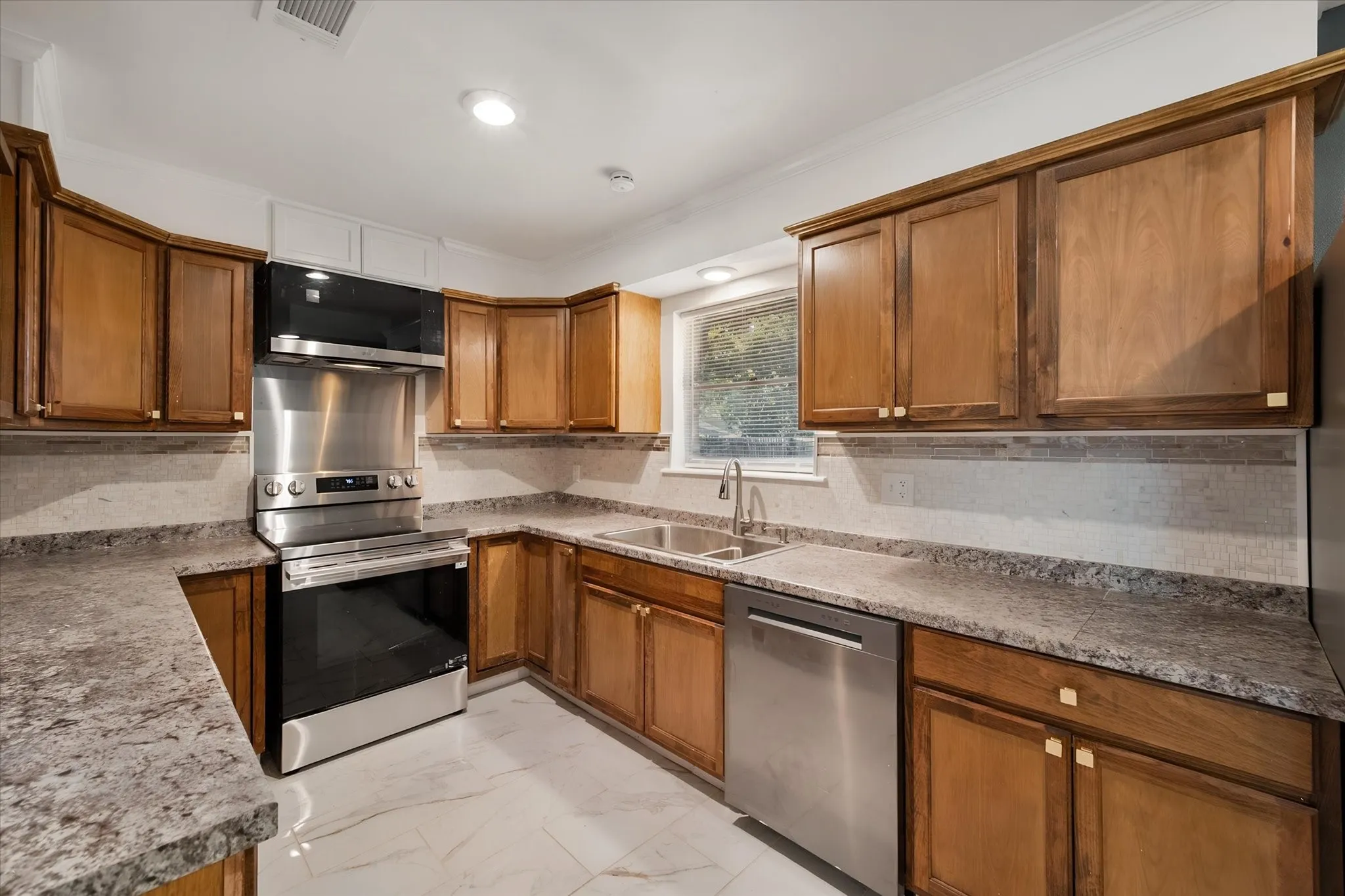 Kitchen with wood-finish cabinetry, stainless steel appliances, speckled countertops, and a tile backsplash