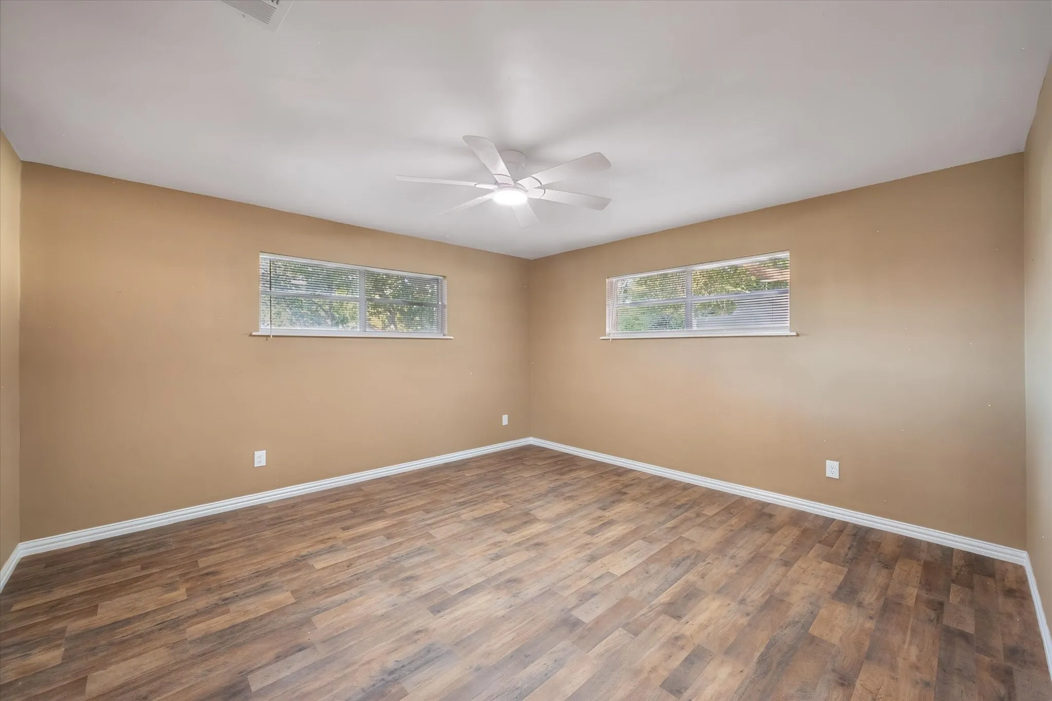 Wood-finish flooring, two windows, and a ceiling fan with integrated lighting