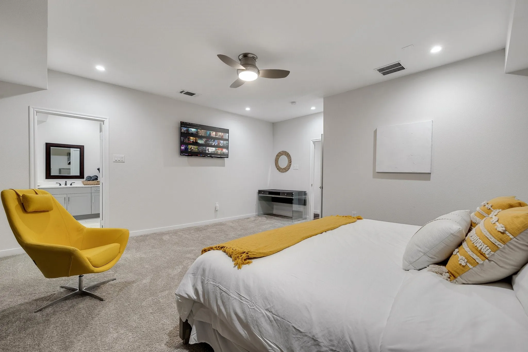 Primary bedroom suite featuring a platform bed with white bedding, carpeted flooring throughout, ceiling fan with integrated lighting, recessed ceiling lights, and a dedicated sitting area with upholstered accent chair
