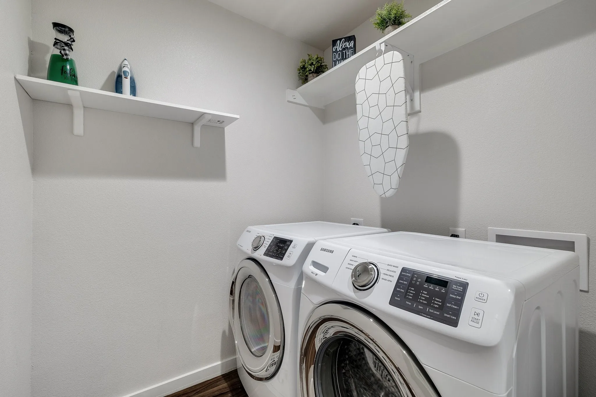 Dedicated laundry room featuring side-by-side front-load washers and dryers with digital controls, white finishes, and wood-finish flooring