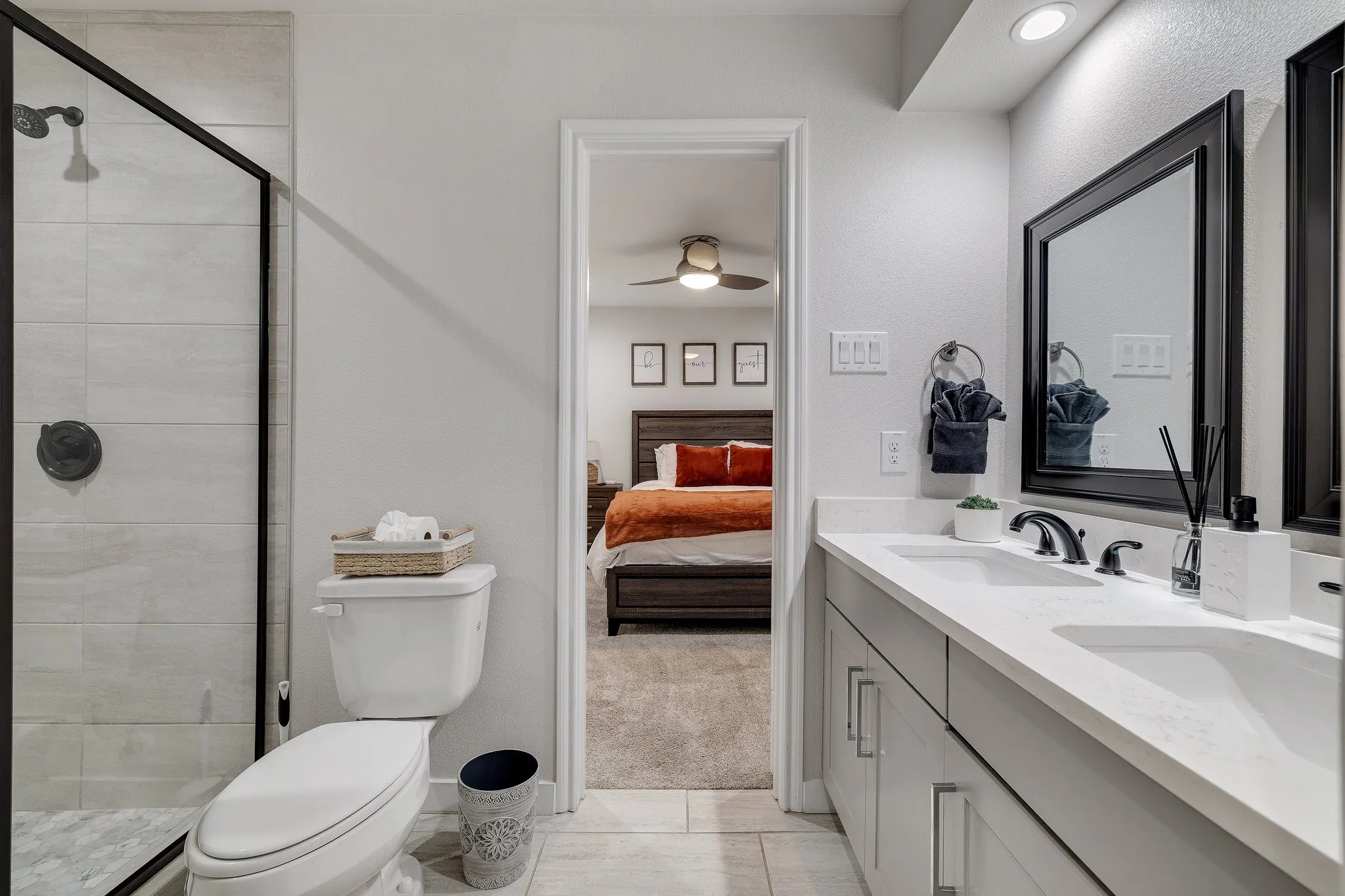 Modern primary bathroom featuring dual vanity with white quartz countertop, matte black hardware and framing, large framed mirror, and tile flooring