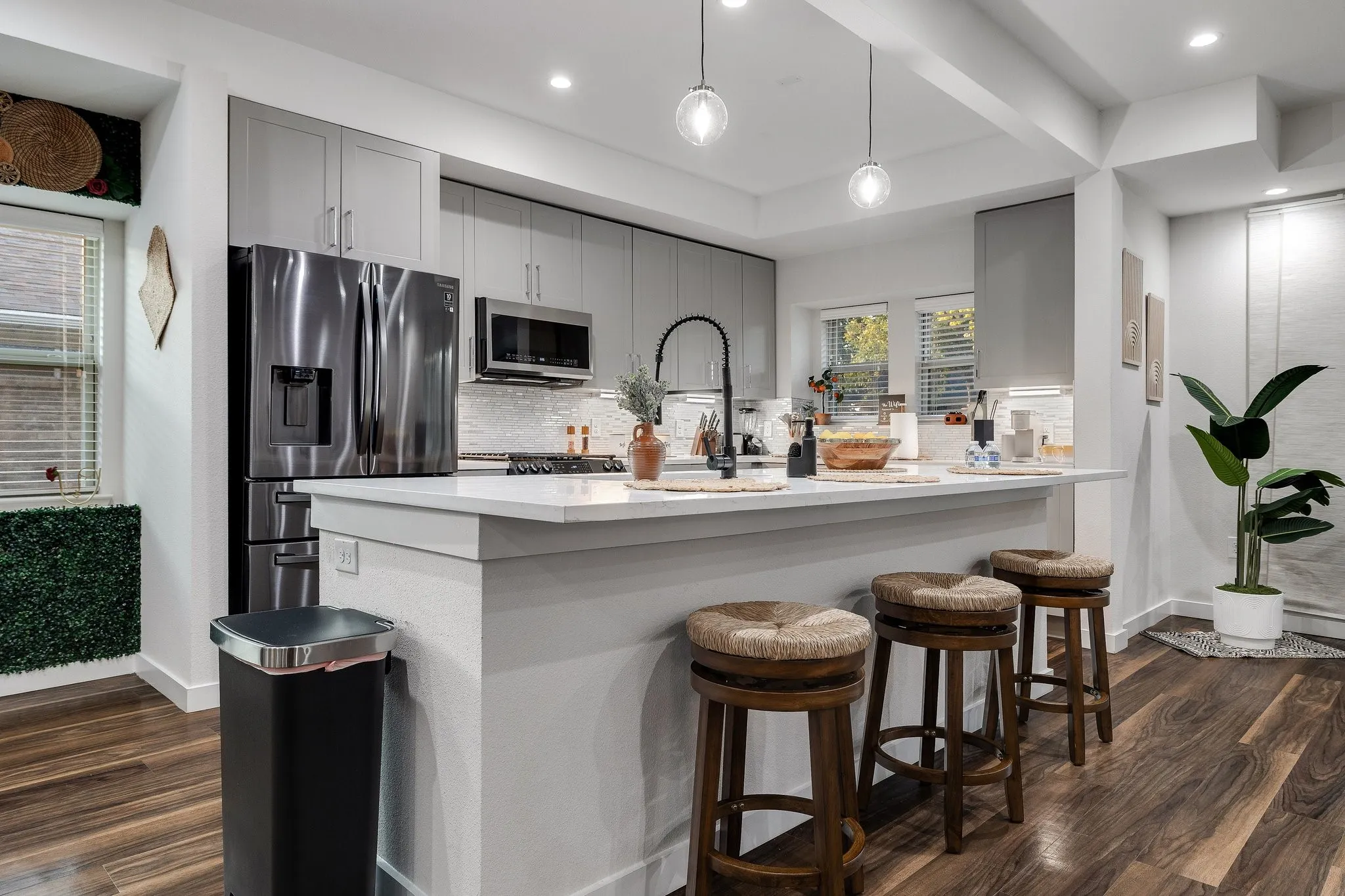 Contemporary kitchen featuring light gray cabinetry, stainless steel appliances, a white island with seating, pendant lighting, and wood-finish flooring