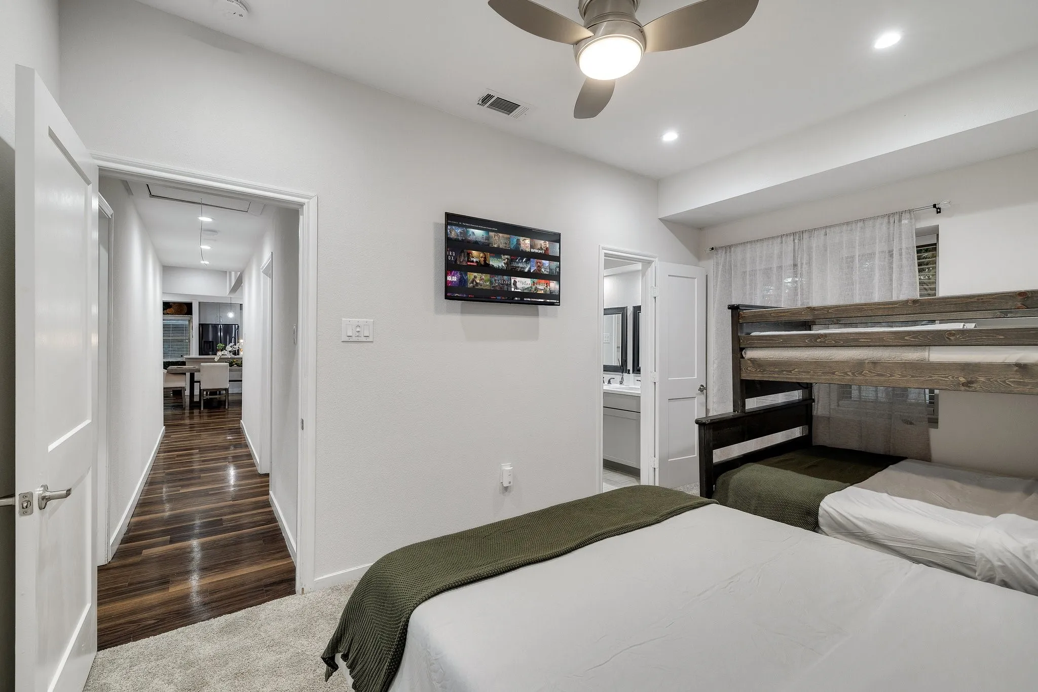 Spacious bedroom with multiple sleeping areas featuring wood-finish flooring, recessed ceiling lighting, and ceiling fan