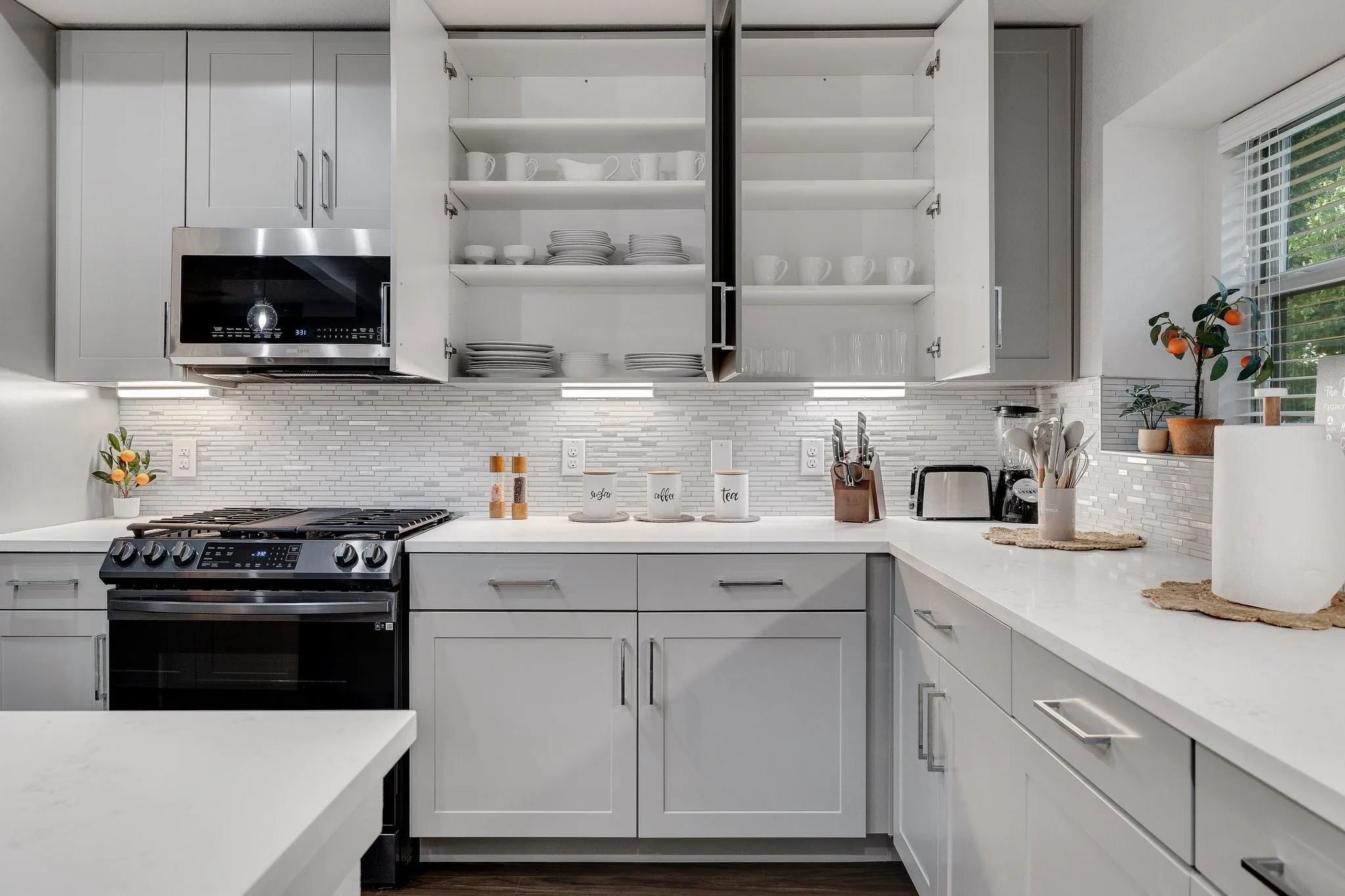 Contemporary kitchen featuring light gray cabinetry, a mosaic tile backsplash, stainless steel microwave, and white countertops
