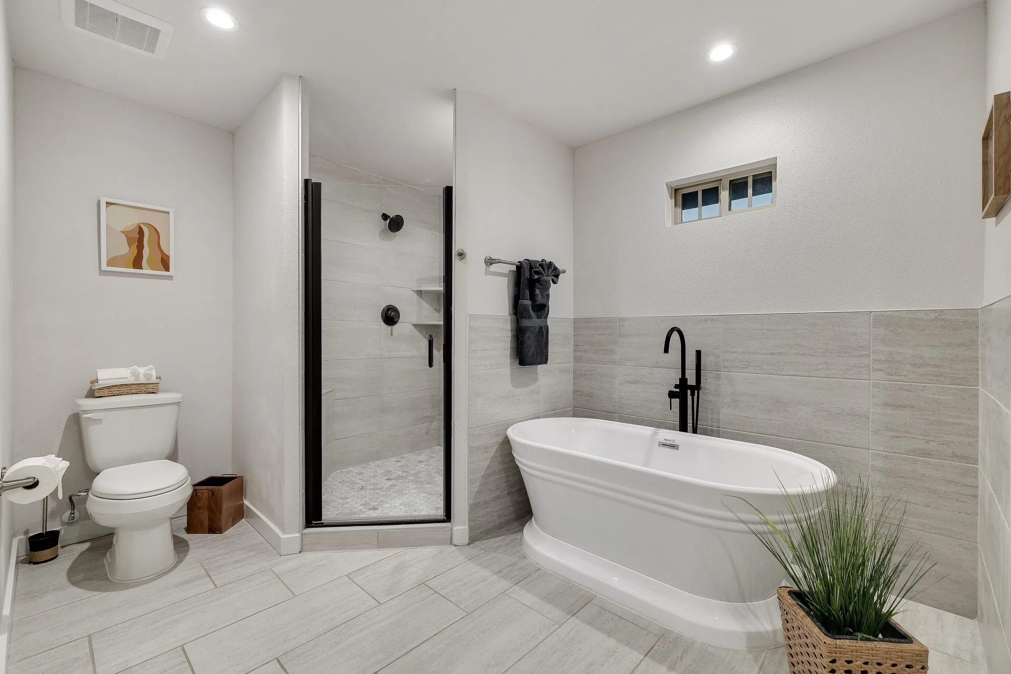 Freestanding soaking tub with a matte black floor-mounted faucet, walk-in shower with matte black fixtures, and light-toned tile flooring