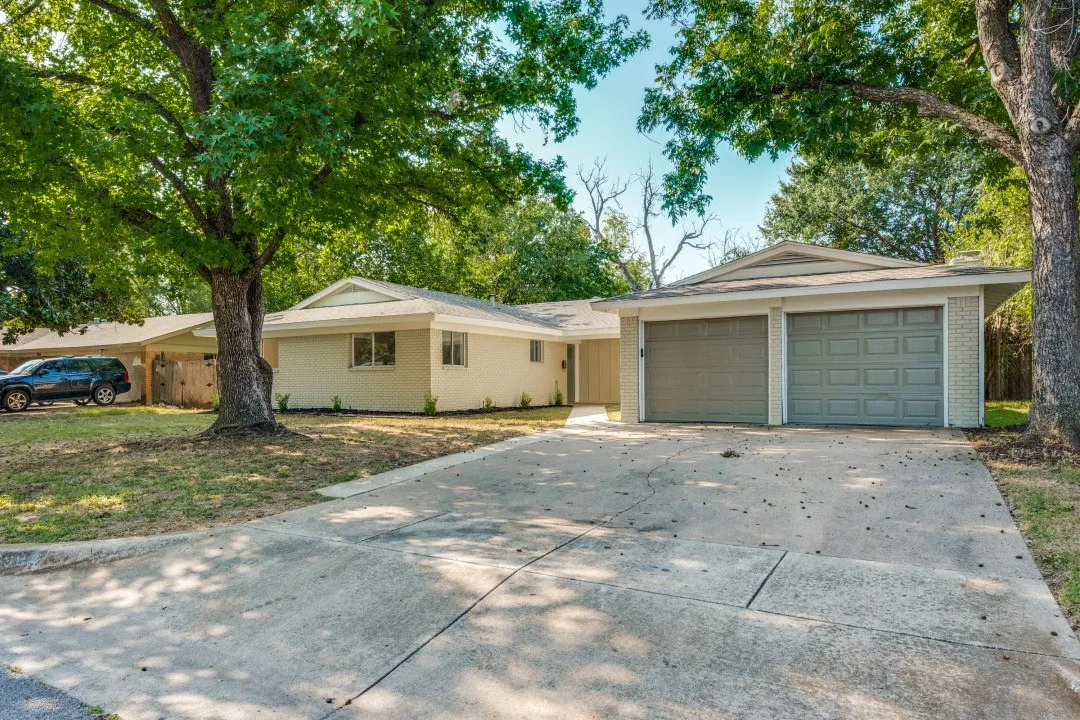 Updated single-story brick home framed by mature shade trees, with a welcoming covered entry, expansive driveway, and attached two-car garage.