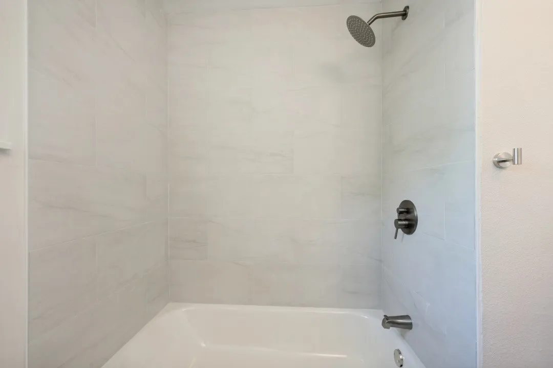 Updated tub and shower combination surrounded by large-format tile and finished with contrasting dark fixtures and a rainfall-style showerhead