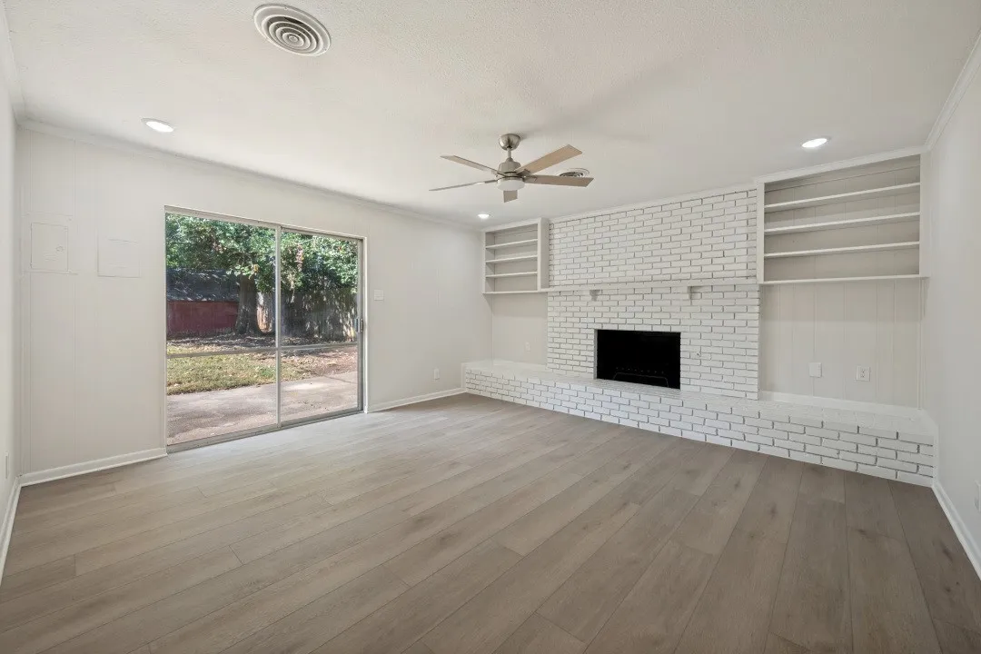 Separate family room anchored by a white-painted brick fireplace with an extended hearth and built-in shelving, is complemented by a ceiling fan and sliding glass doors opening to the backyard.