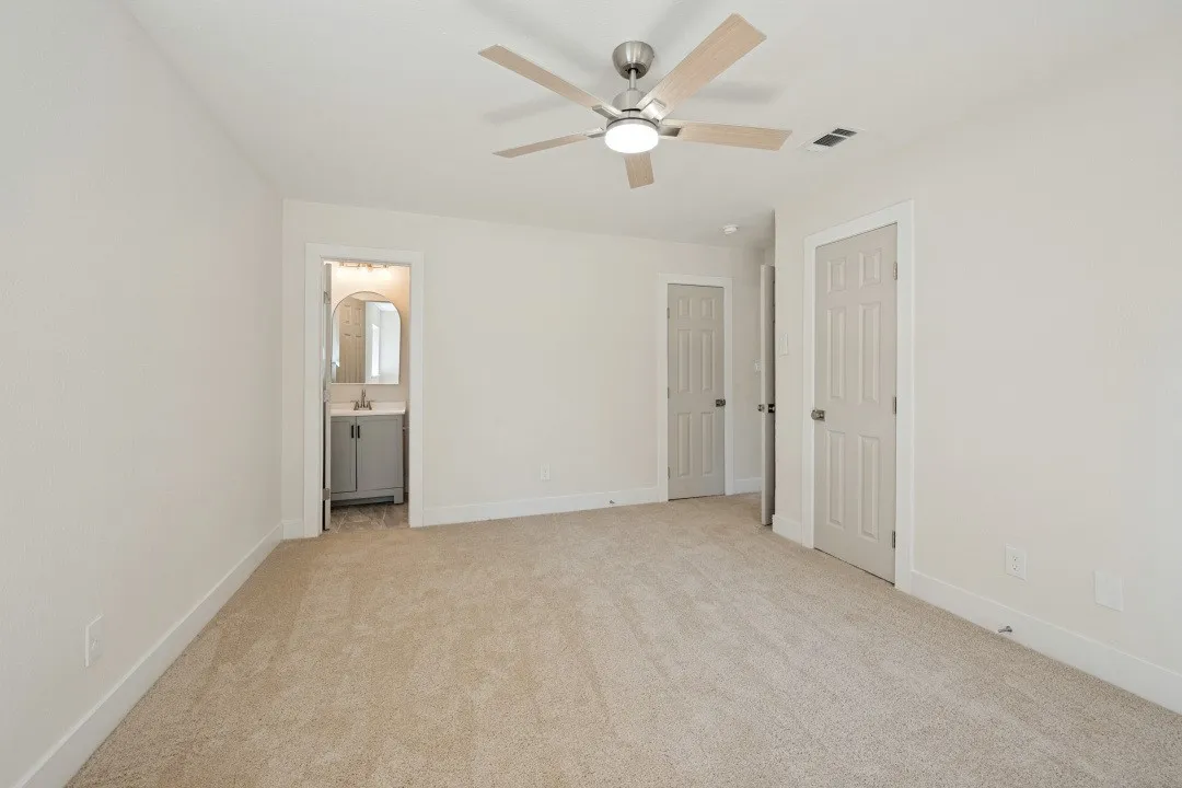 Generously sized primary bedroom with windows on two sides, updated carpet, contemporary ceiling fan, and abundant natural light.