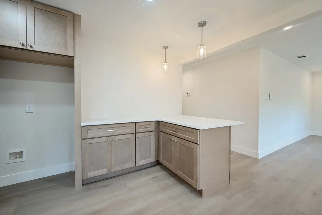 Additional cabinetry and quartz counter space extend beyond the main kitchen, providing useful storage and a convenient serving or beverage area accented by pendant lighting.